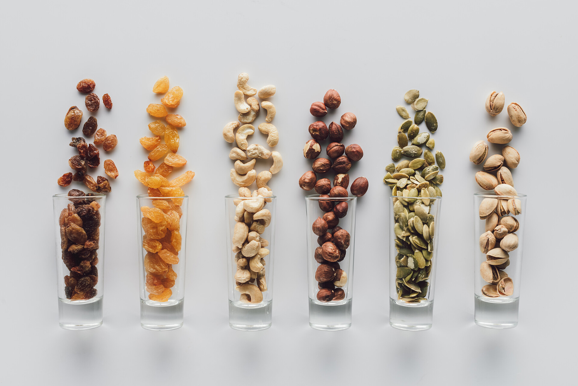 白色背景下的坚果和果干各种美味的坚果和葡萄干在玻璃杯分离的白色背景