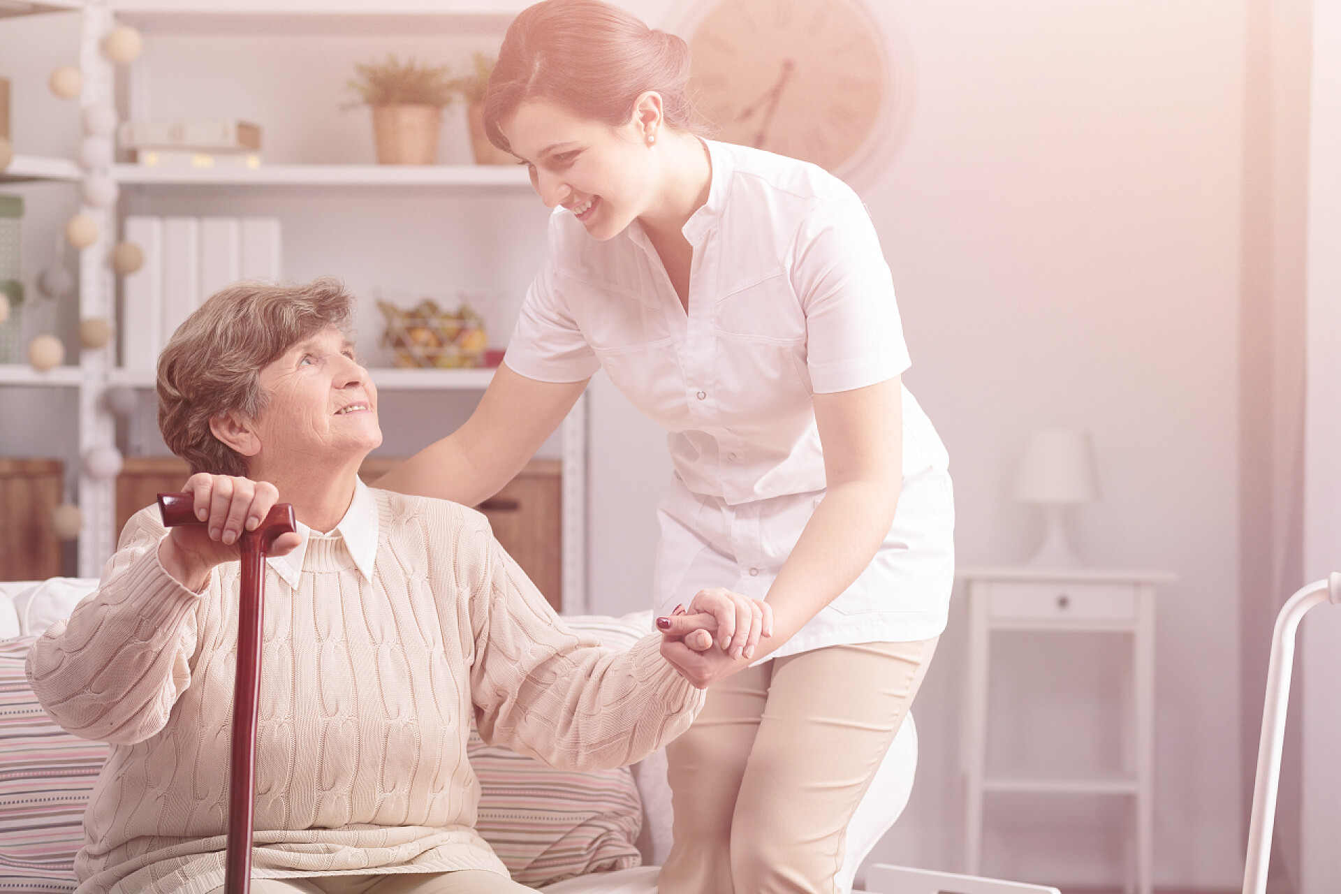 在室内帮助老奶奶起身的女护士帮助照料者支持微笑的资深妇女与手杖