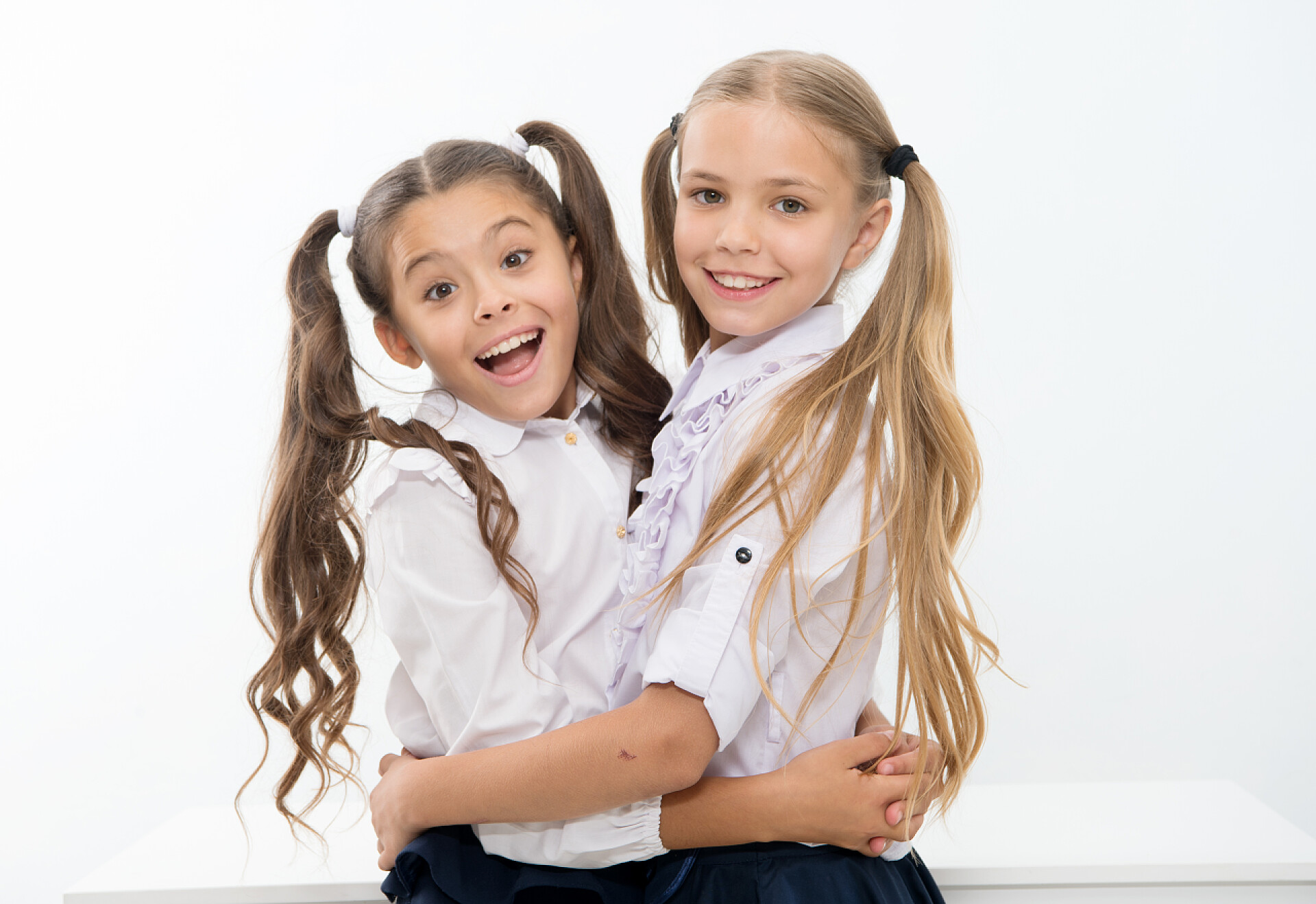 白色背景前拥抱的两个女孩快乐的女朋友互相拥抱,友谊的概念.真正的友谊胜过世界上任何其他关系。快乐的女朋友.