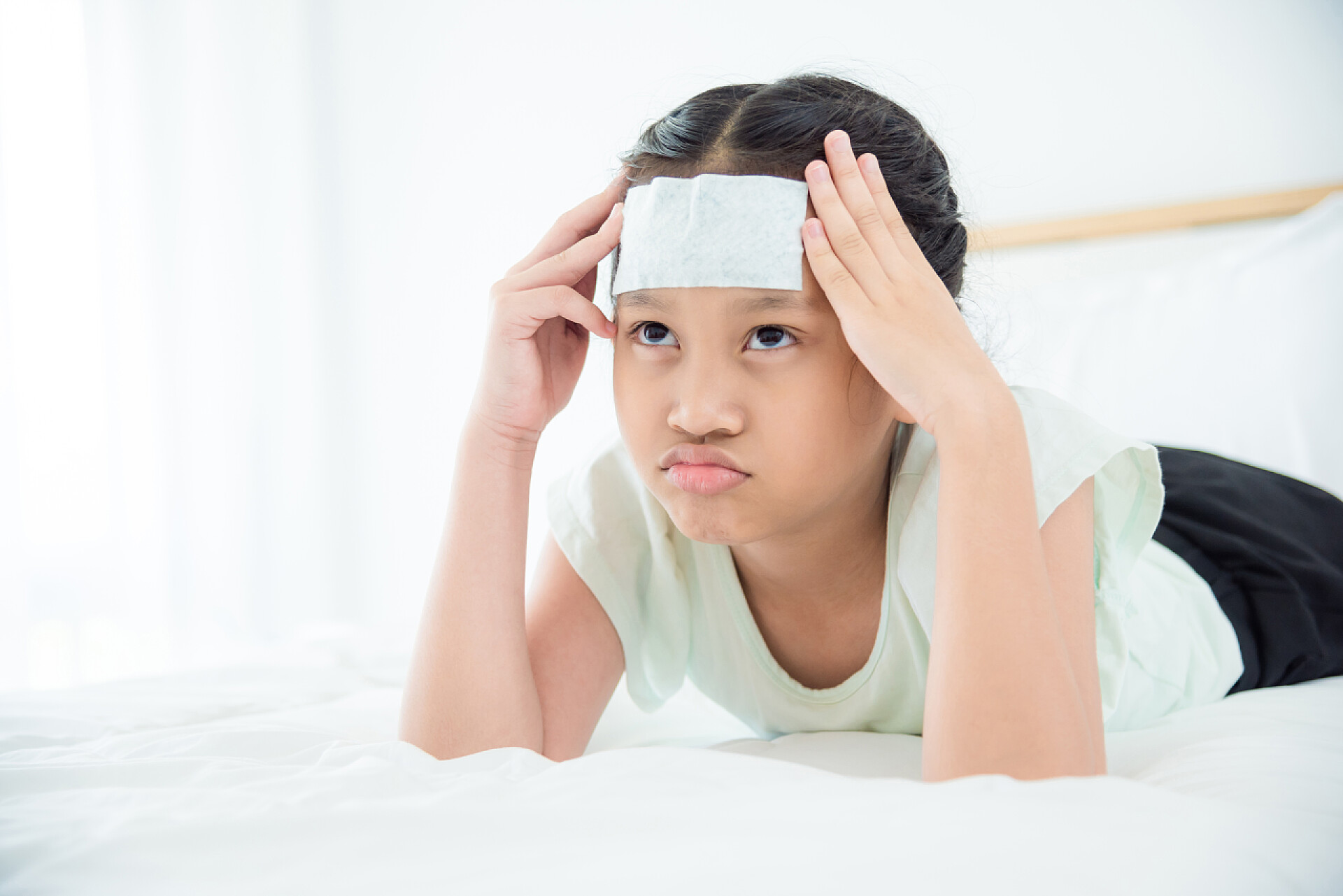 发烧的女孩趴在床上年轻的亚洲与凉爽的凝胶在额头上头痛躺在床上