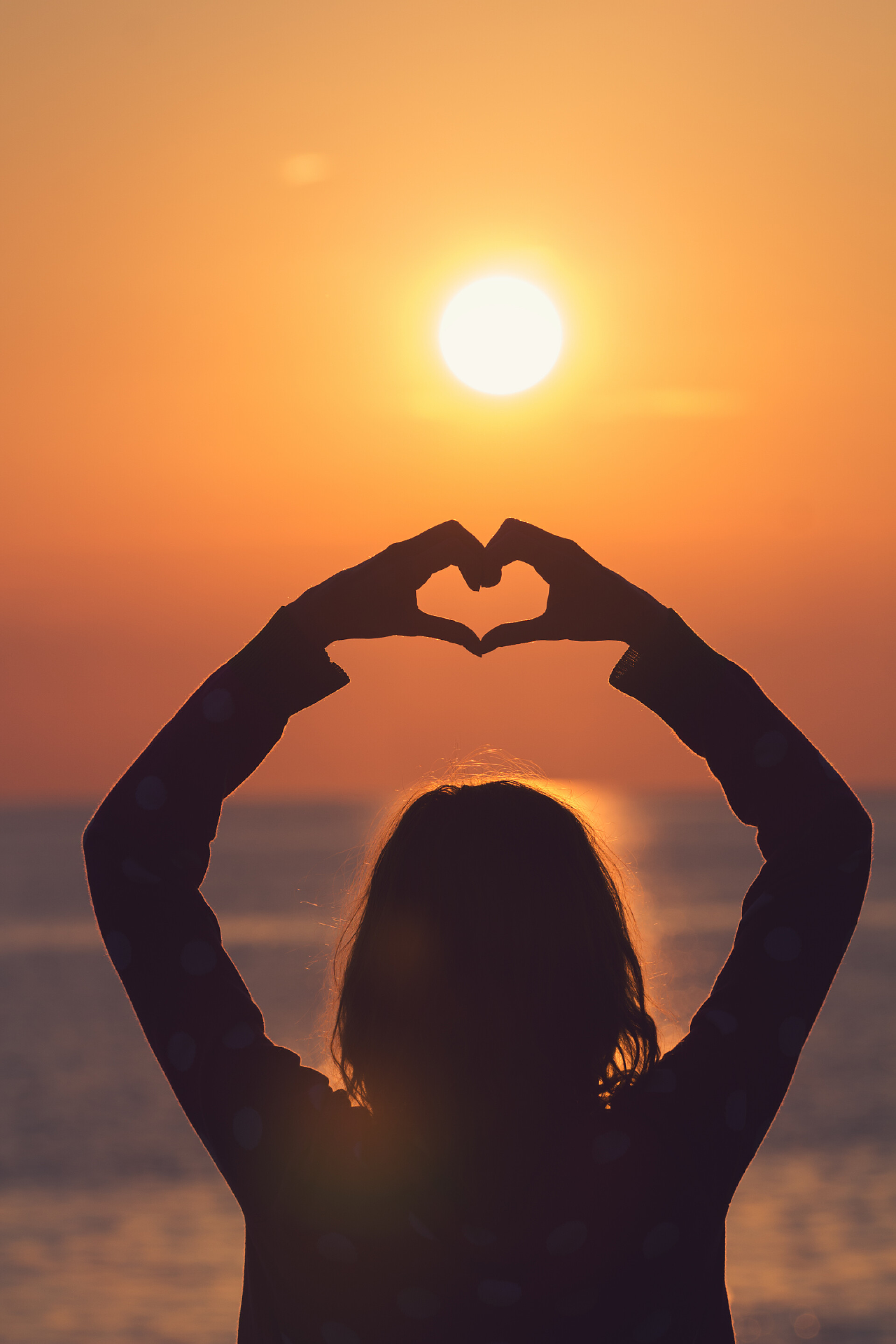 阳光下的美丽女人一个抱着大海/海洋背景的女孩的剪影.