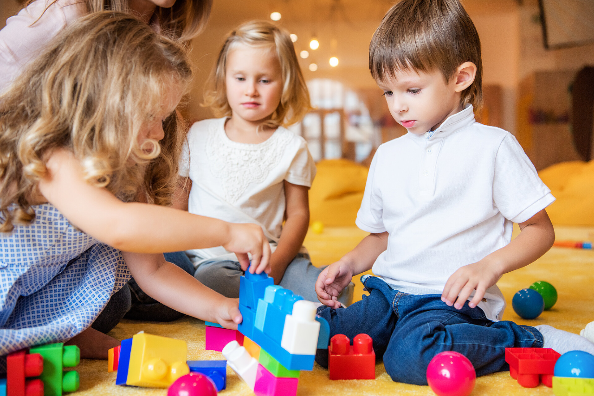 在玩积木的三个小孩子和陪伴的老师可爱的孩子们在幼儿园的地板上玩建设者