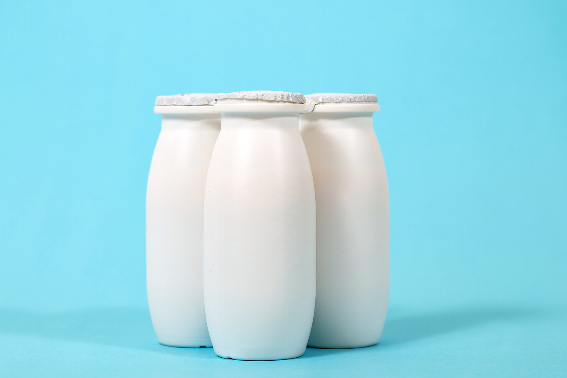 蓝色的背景墙有三瓶牛奶在白色背景查出的液体酸奶瓶.