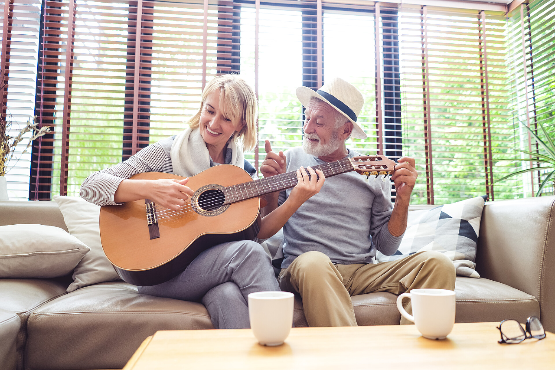坐在沙发上的一对老夫妻爱着坐在沙发上的成熟夫妇, 妻子一边弹吉他, 一边在客厅里一起唱歌