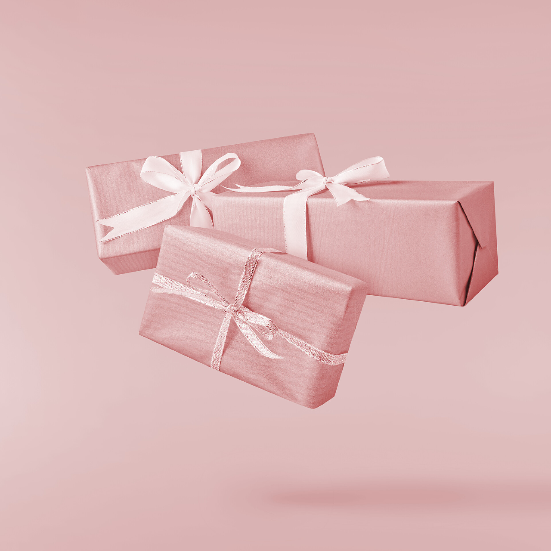 粉色背景下的三个粉色礼物盒圣诞节的概念。创意圣诞构想, 通过下降在空气礼品盒超过粉红色的背景。最小的概念