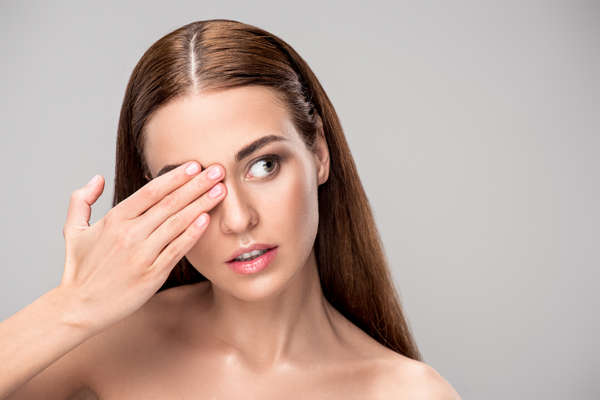 在灰色背景前的一个美女美丽的黑发女孩的肖像闭上一只眼睛, 隔离在灰色