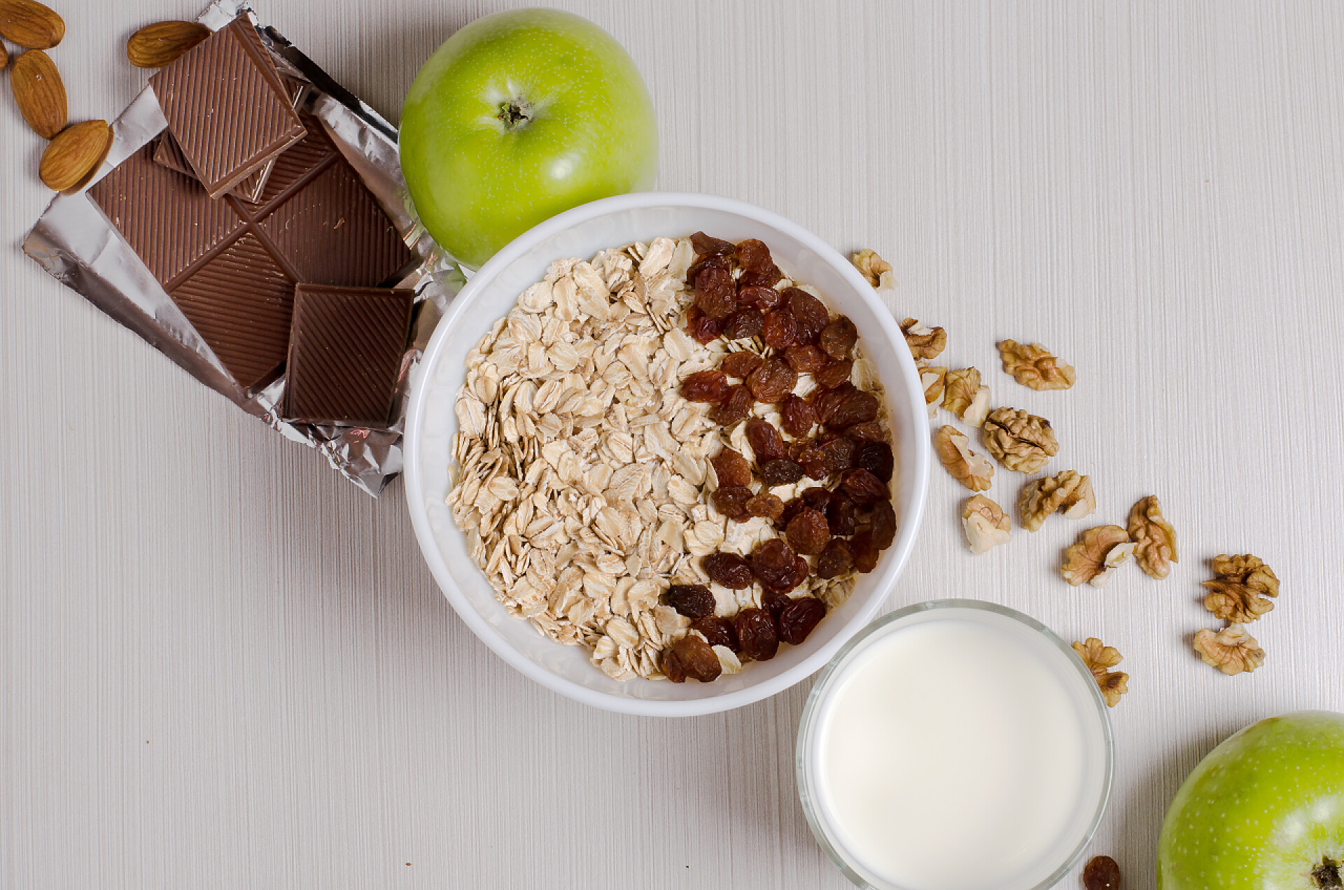 在白色桌子上的燕麦片早餐健康早餐。燕麦片配葡萄干和酸奶。牛奶在杯子里。巧克力, 水果, 白色桌子上的坚果。平顶竞争