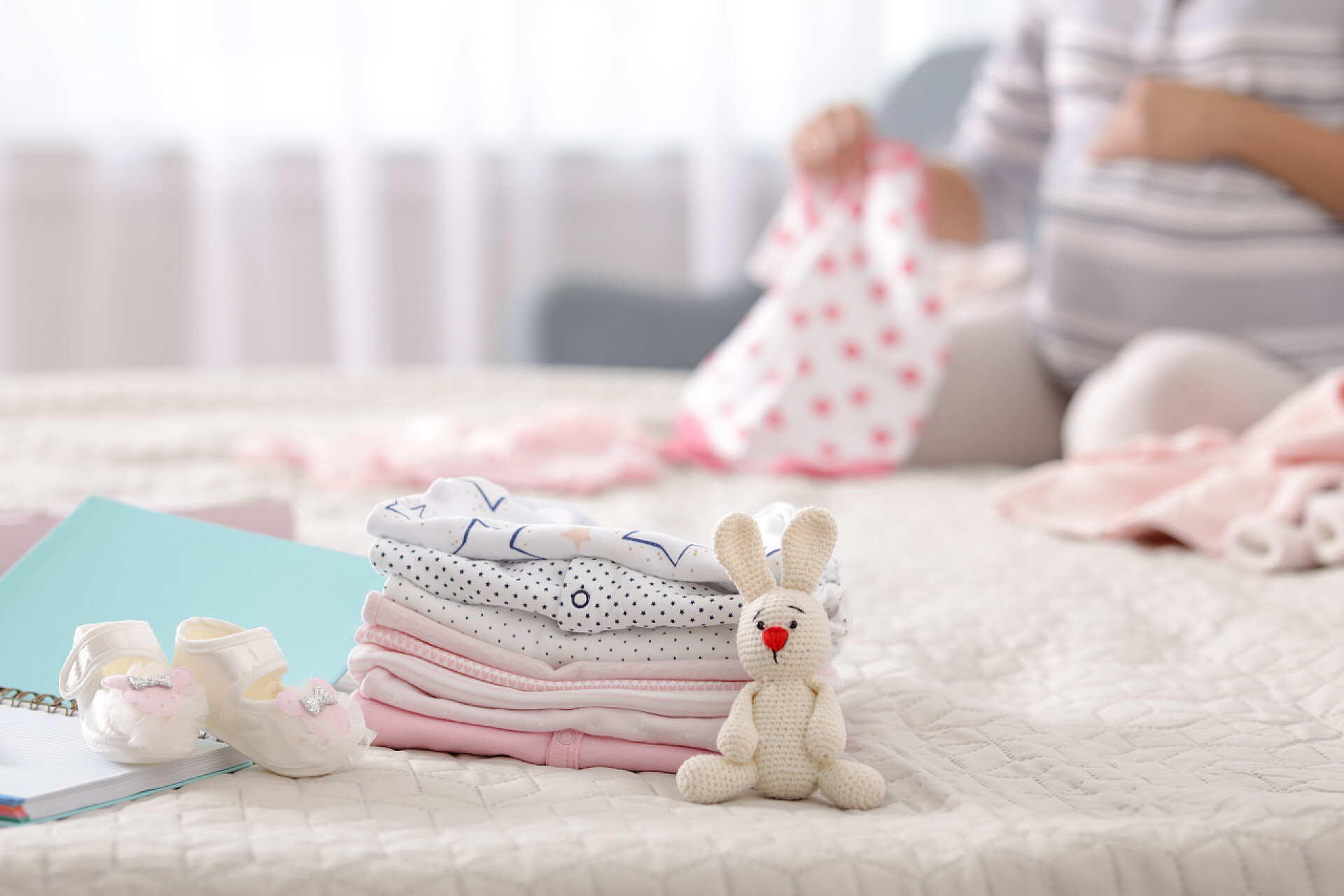 坐在床上整理即将出生的婴儿衣服的妈妈为妇产医院和有背景的孕妇准备的婴儿衣服