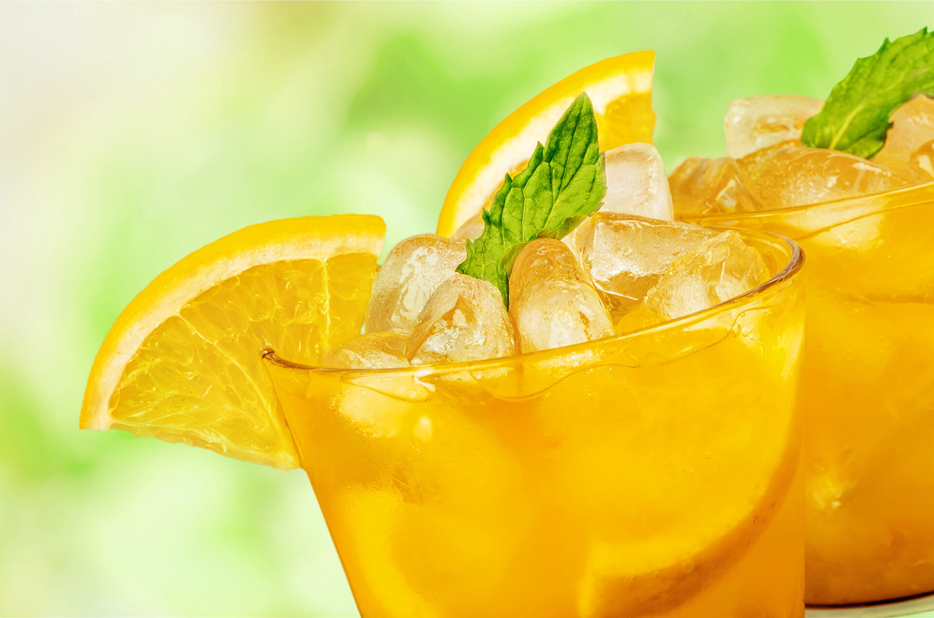 在绿色的背景下两杯装着橙色的饮料的杯子背景橙色夏季鸡尾酒 