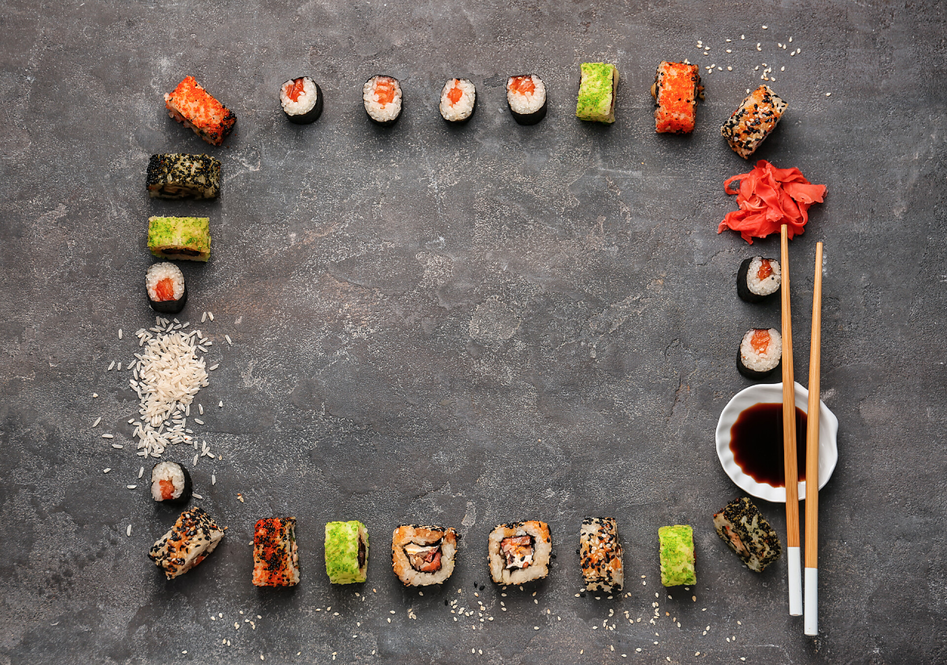 灰色的桌子上围着一排寿司和蘸料还有筷子灰色背景上由不同寿司制成的框架