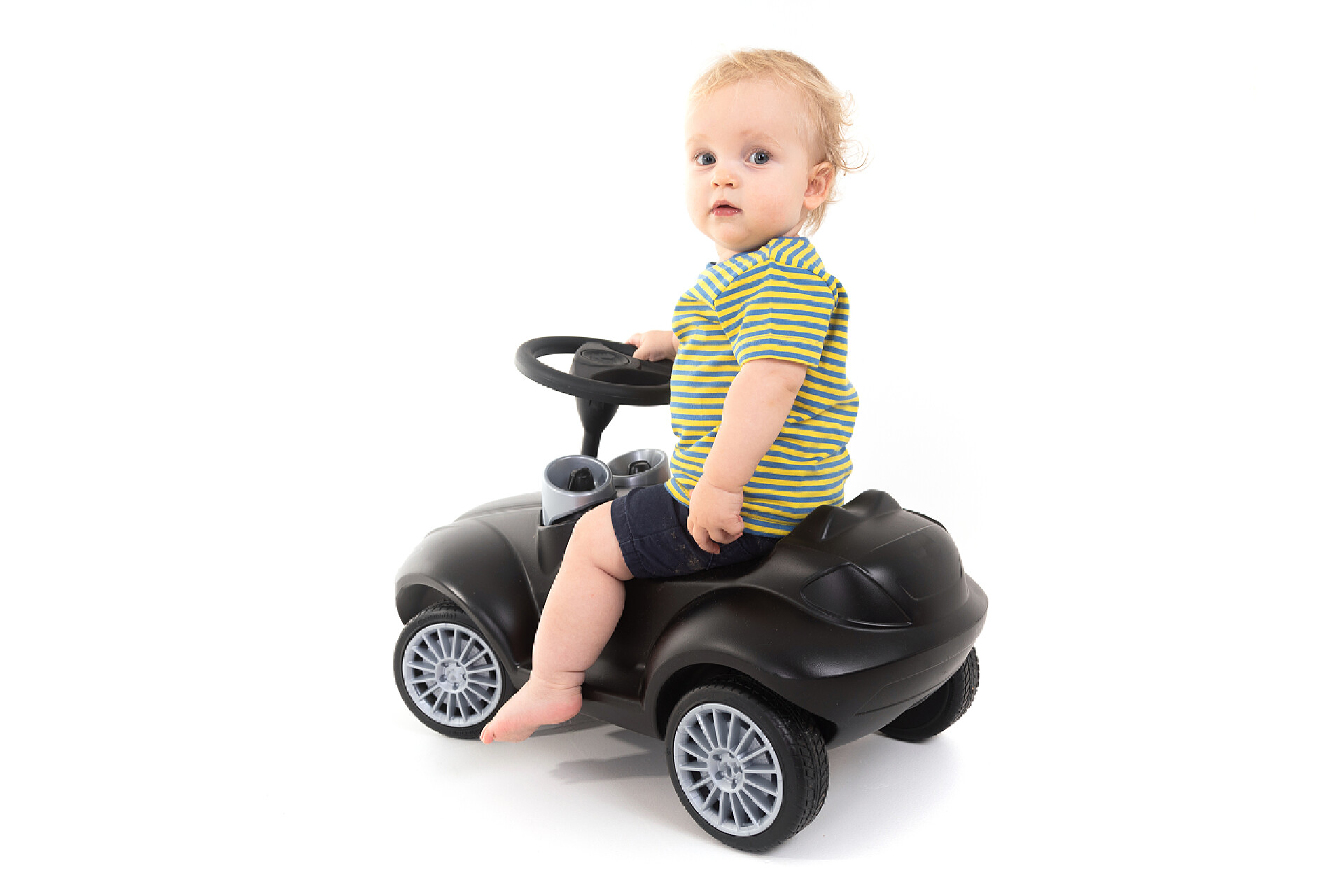 在白色背景下一个穿着绿色短袖的小孩子在开着黑色小车儿童坐在被隔绝的轮床在白色背景