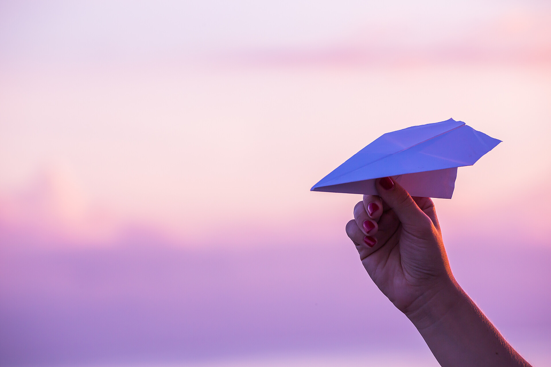 在紫色的背景下一个人手拿着纸飞机纸飞机反对日落天空