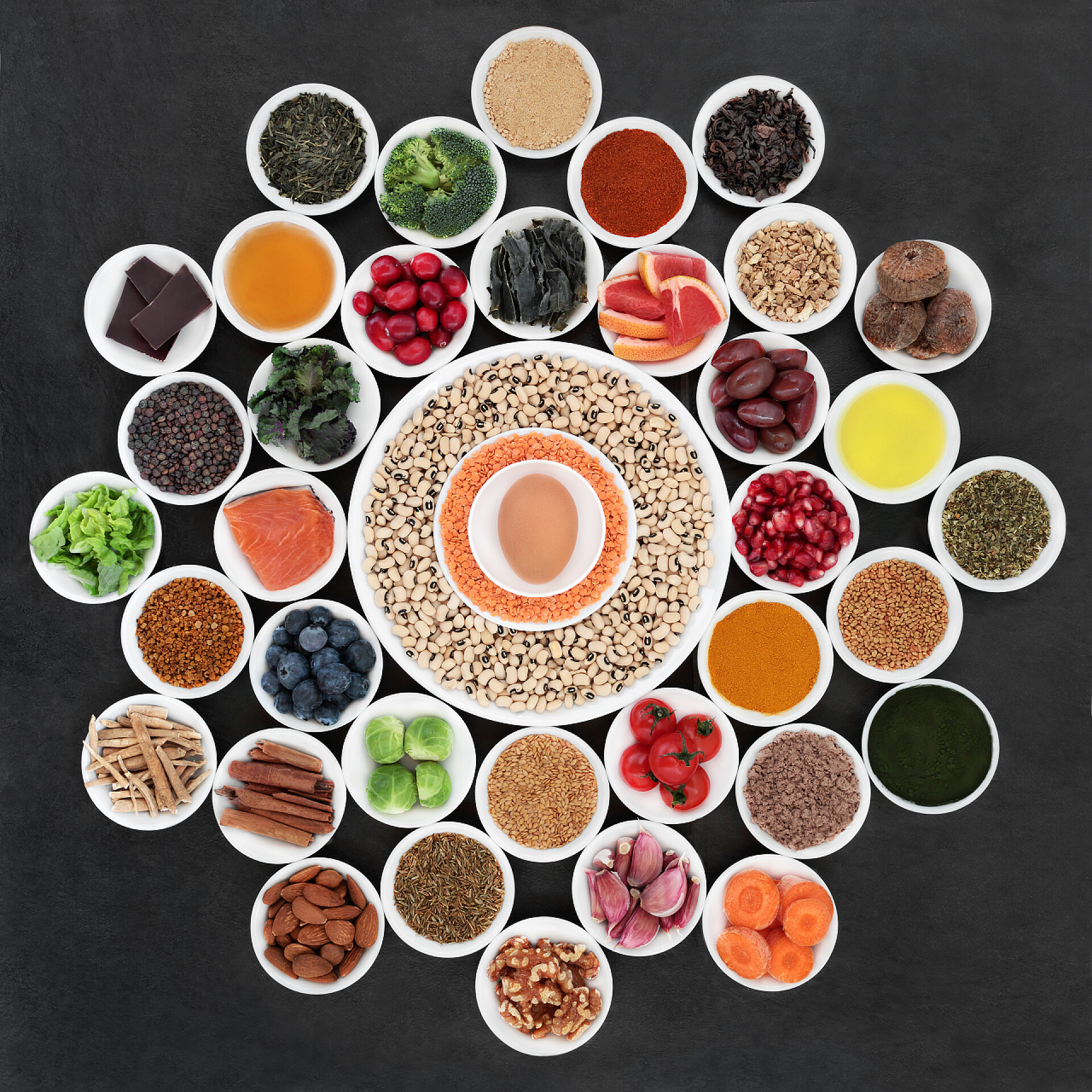 在黑色的桌子上显示着不同种类的果蔬和调料大型保健食品车轮与食品, 以减缓衰老过程。富含抗氧化剂、花青素、膳食纤维和维生素。在石板背景顶视图上.