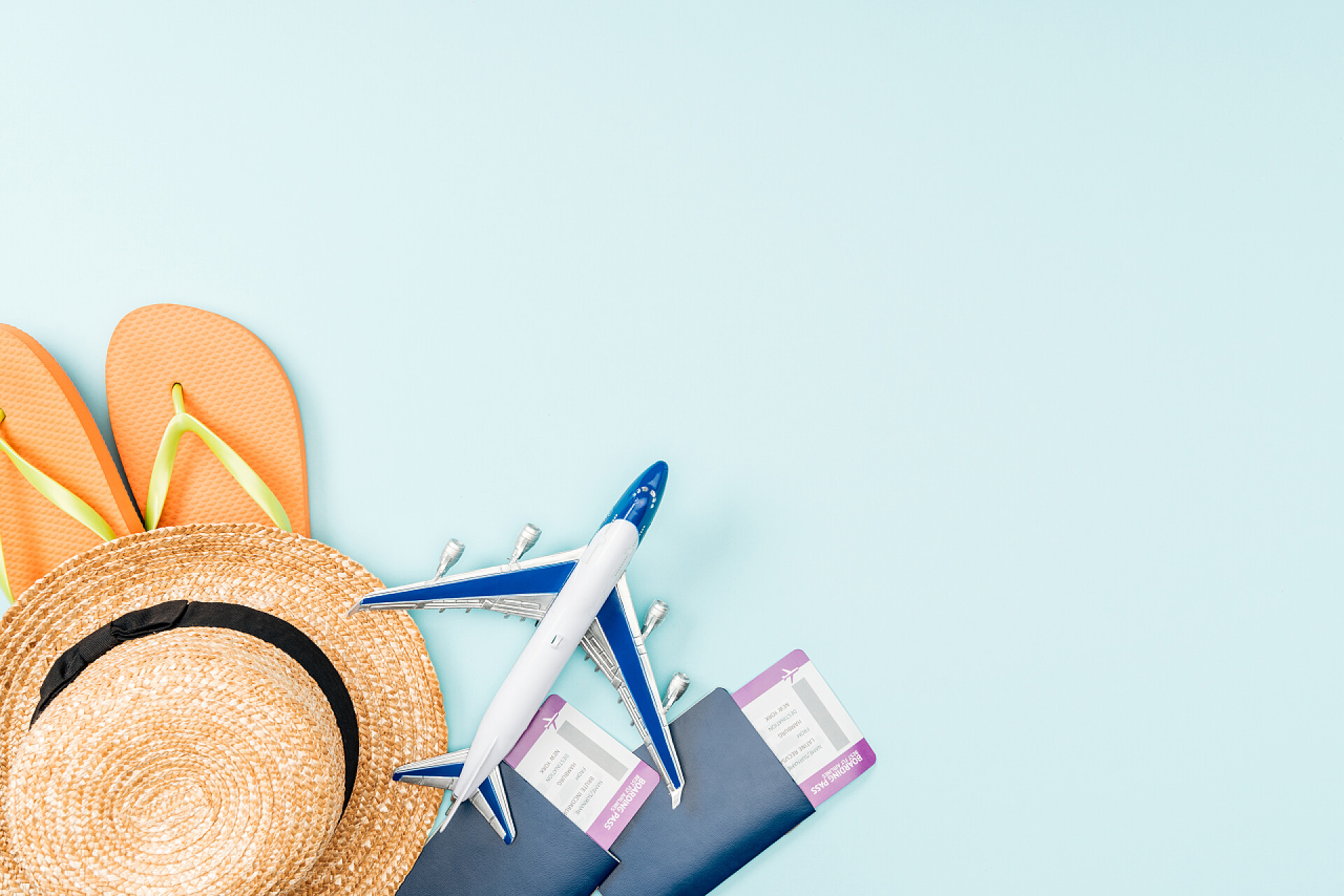 蓝色背景下的用品蓝色背景上的护照、机票、草帽、翻盖和玩具飞机的顶视图 