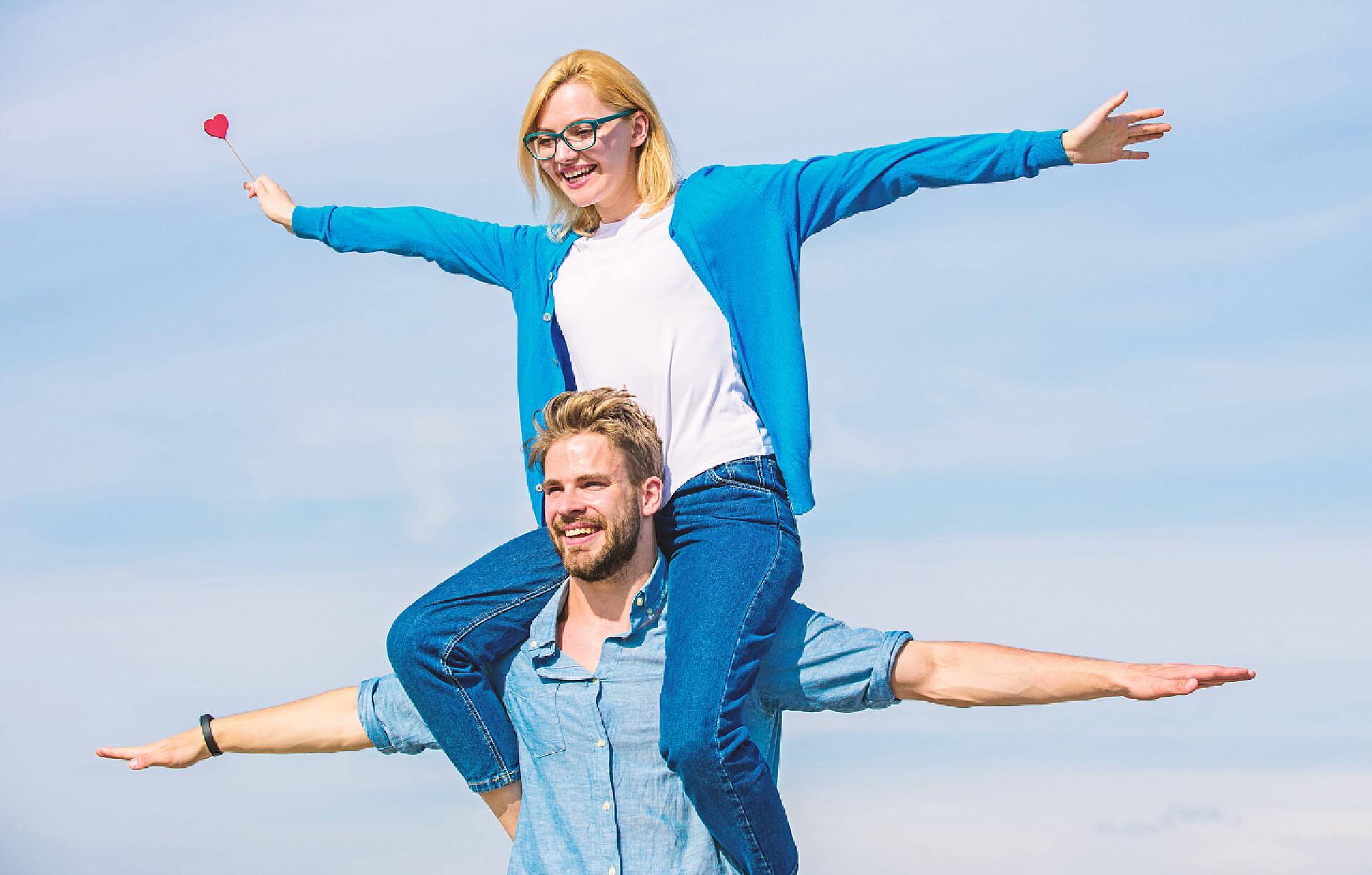 蓝天白云下一对恩爱的情侣自由概念。情侣在爱中享受自由的户外阳光明媚的一天。夫妻俩快乐的日子一起玩。男人扛着女朋友的肩膀, 天空的背景。恋人享受约会和感觉自由