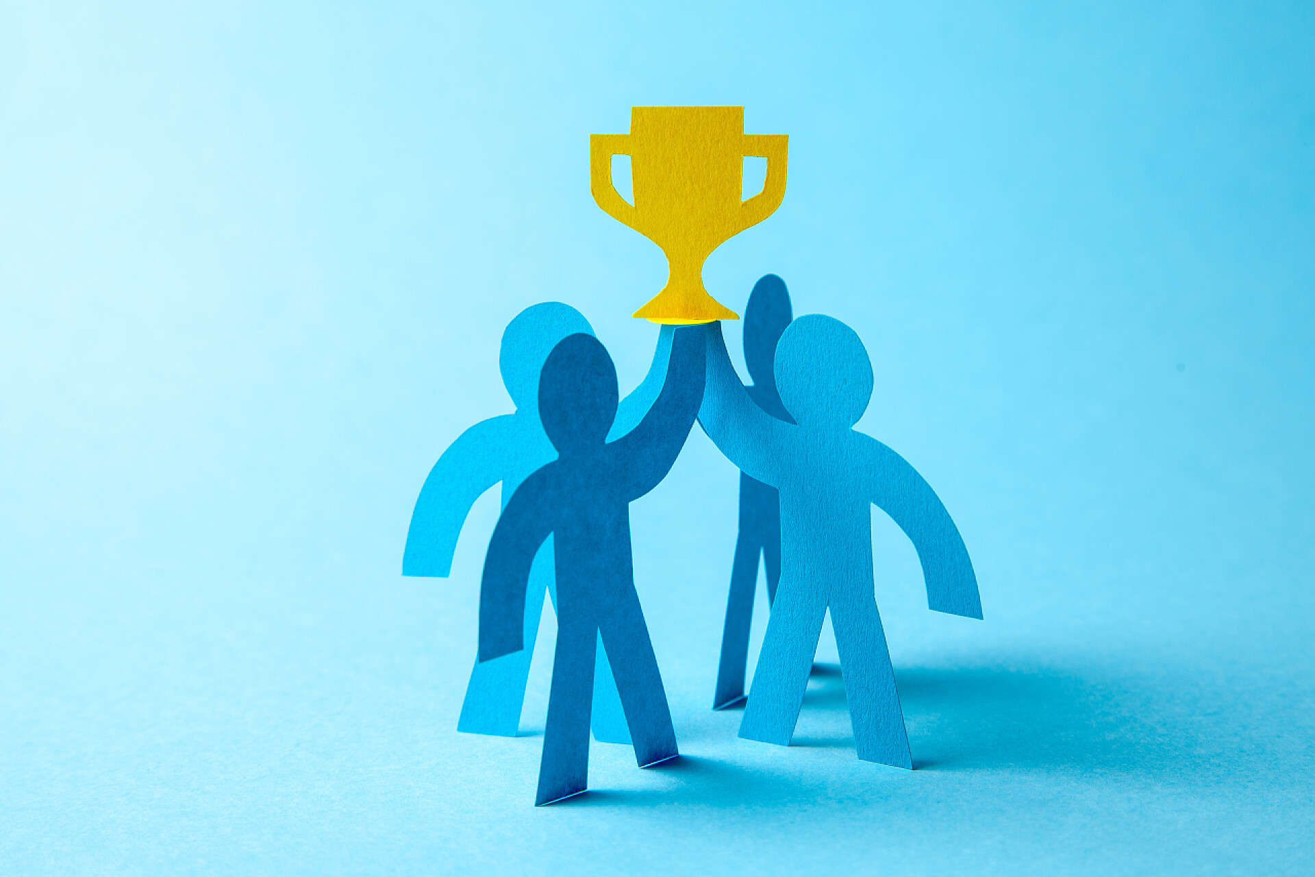 蓝色背景下四个蓝色的小卡片人举着黄色的奖杯成功的商业团队冠军手里拿着金杯。团队建设。领导者和工人实现目标.