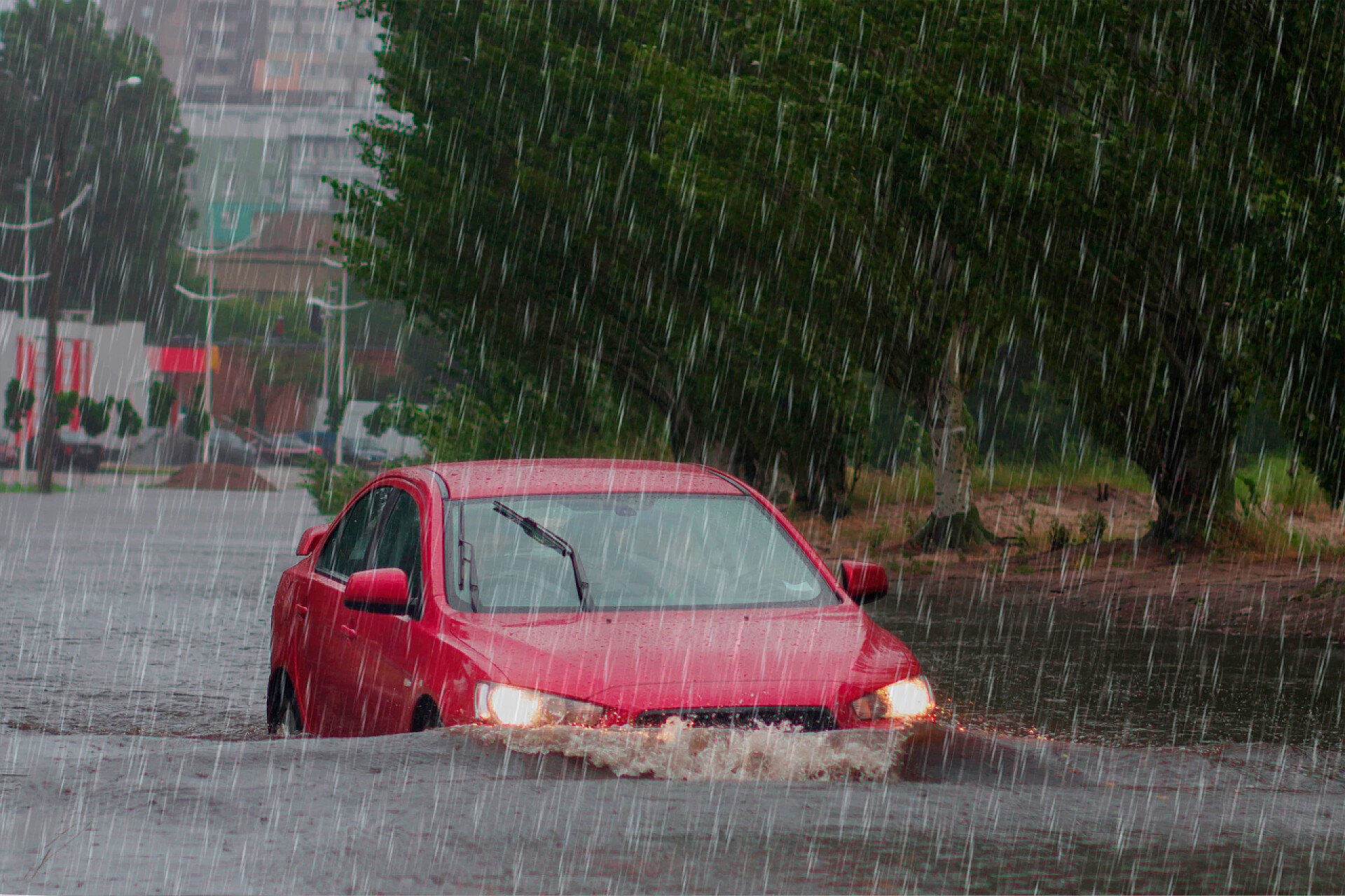 在瓢泼大雨的水面上行驶着红色的轿车汽车运动雨水从车轮上喷出一大团水花