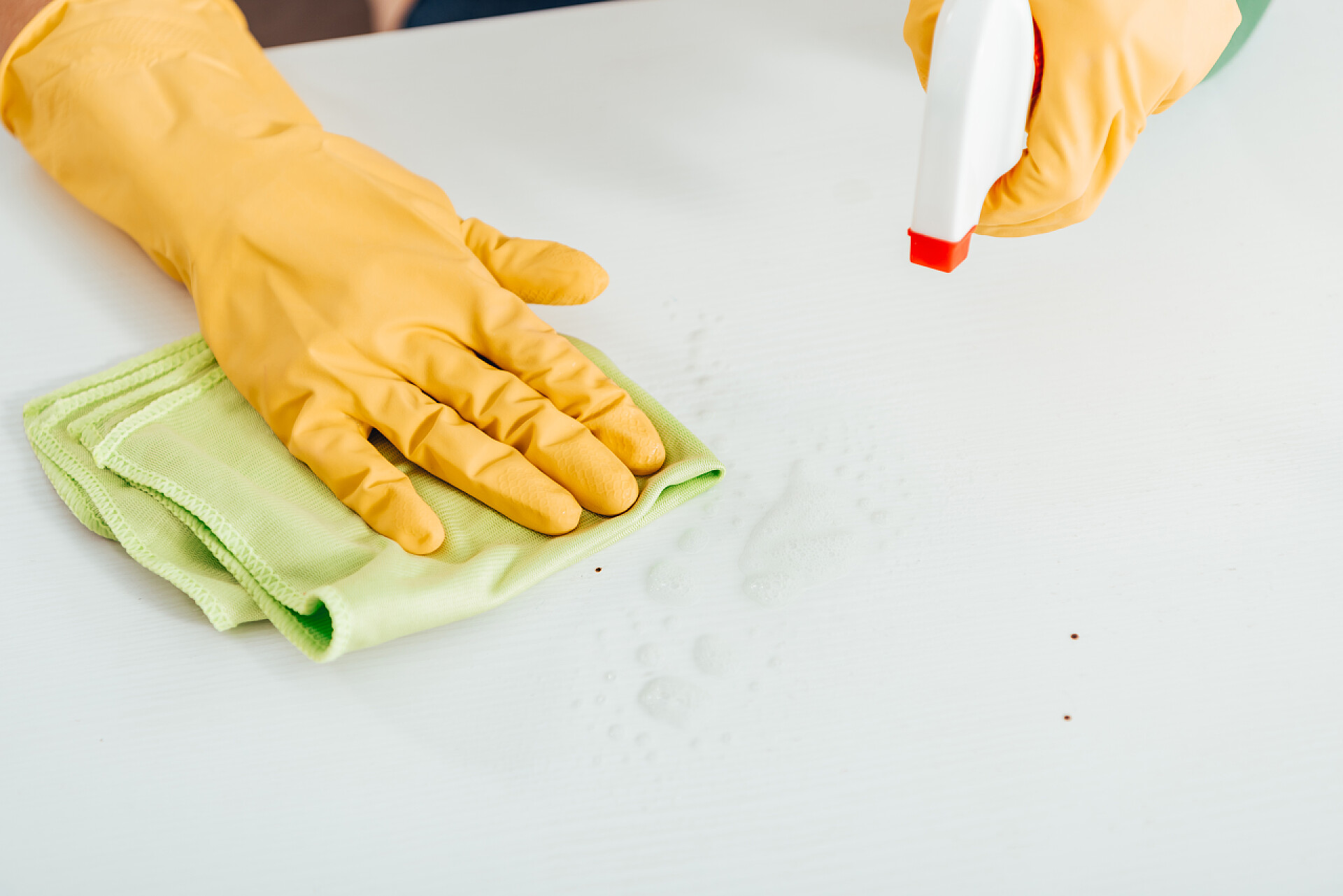 戴着黄色手套的女人用清洁剂在擦着白色的桌子妇女的裁剪的看法妇女在黄色橡胶手套清洁白色表面用抹布和喷雾