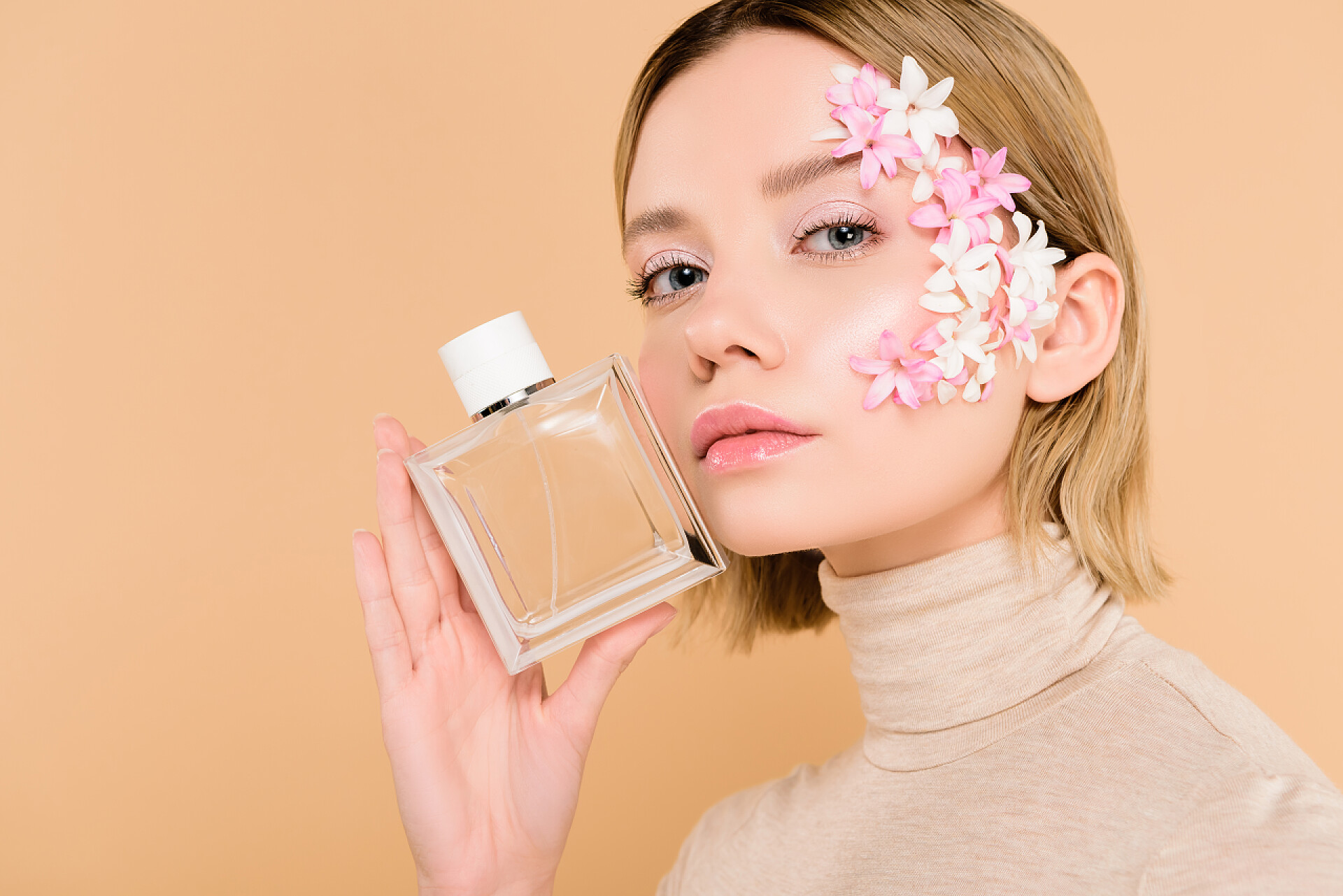 橙色背景墙前一个女人拿着香水在展示美丽的女人与鲜花在脸上举行一瓶香水隔离在米色