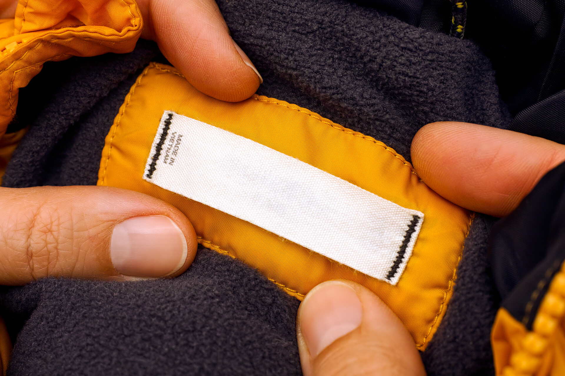 一双手把衣服领子的尺码标展露出来妇女手拿着黄色夹克与衣服标签。特写.