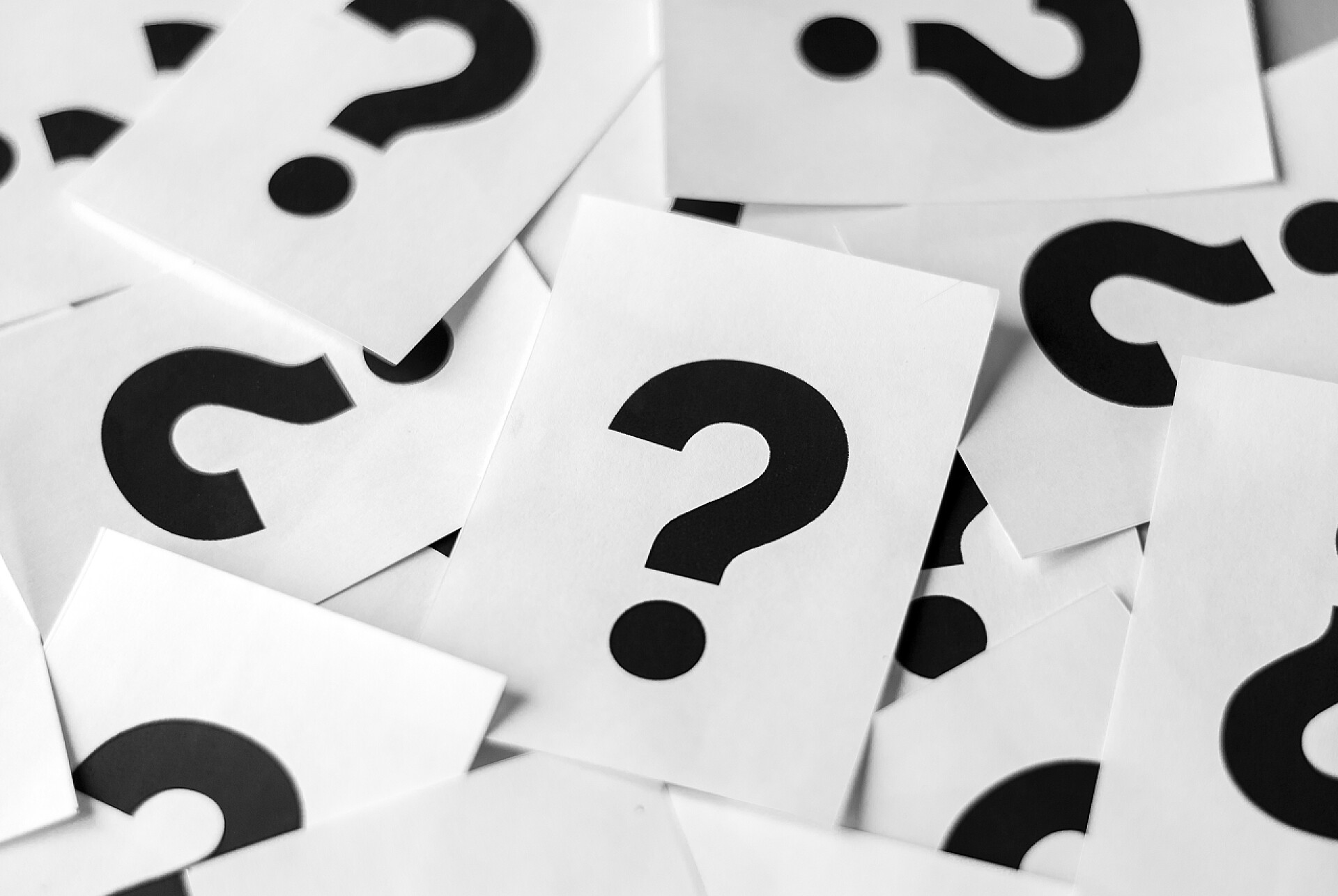 在桌子上的白色纸张和黑色问号成堆的白色卡片, 带有黑色问号, 近距离, 全框架垂直背景概念