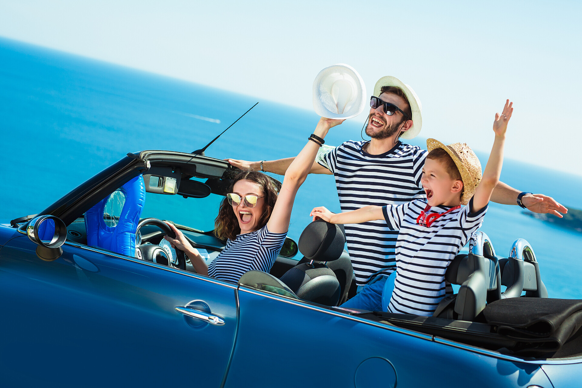 蓝天下一家三口开着敞篷车去自驾游幸福的家庭乘汽车去大海。人们在开心的敞蓬车。夏季度假概念