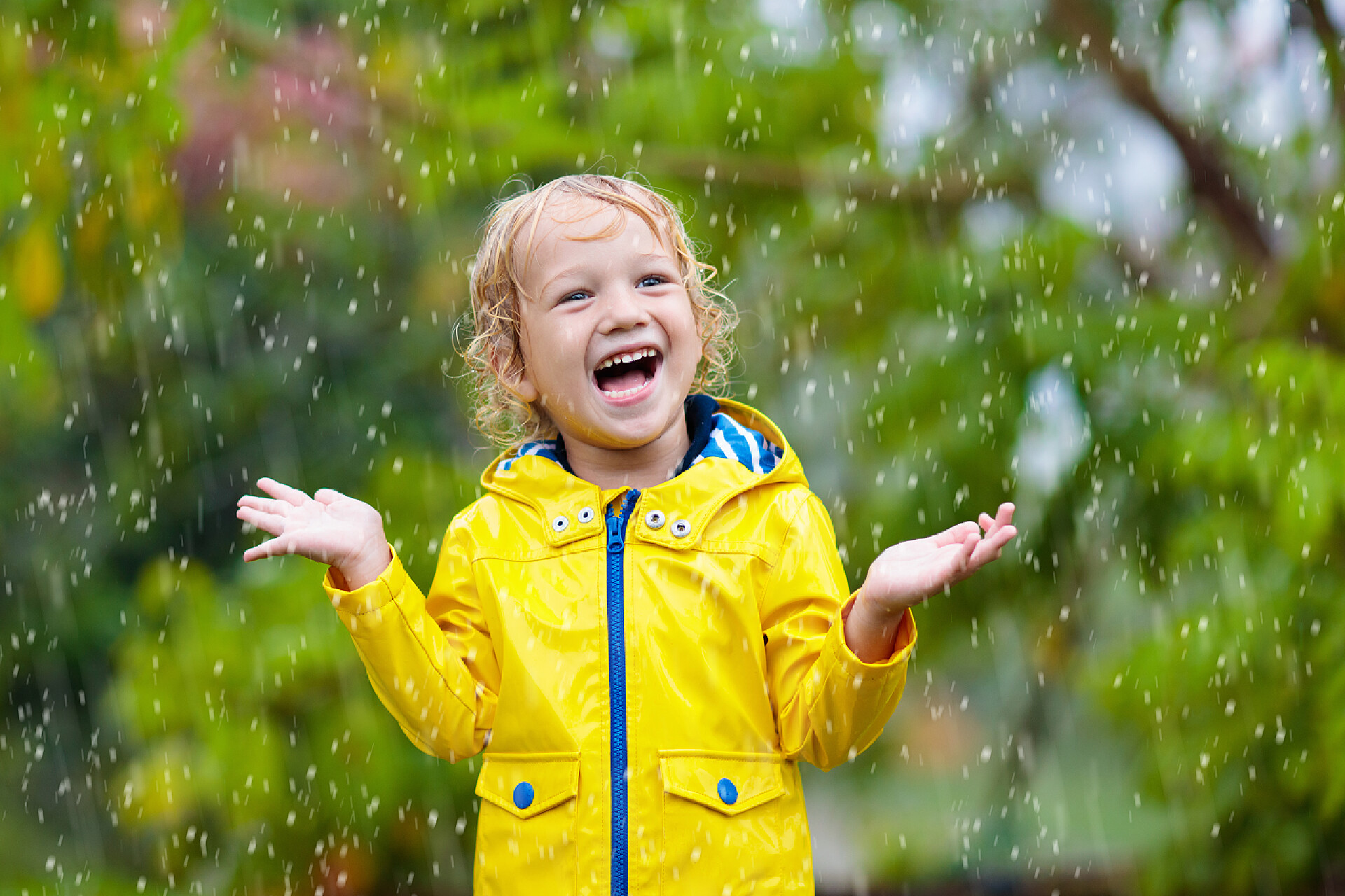 一个穿着黄色上衣的金发孩子在雨中嬉戏孩子们在秋雨中玩耍。孩子们在雨天在户外玩耍。小男孩在大雨中雨点。公园里的秋天风暴。儿童防水服。任何天气下的户外儿童.