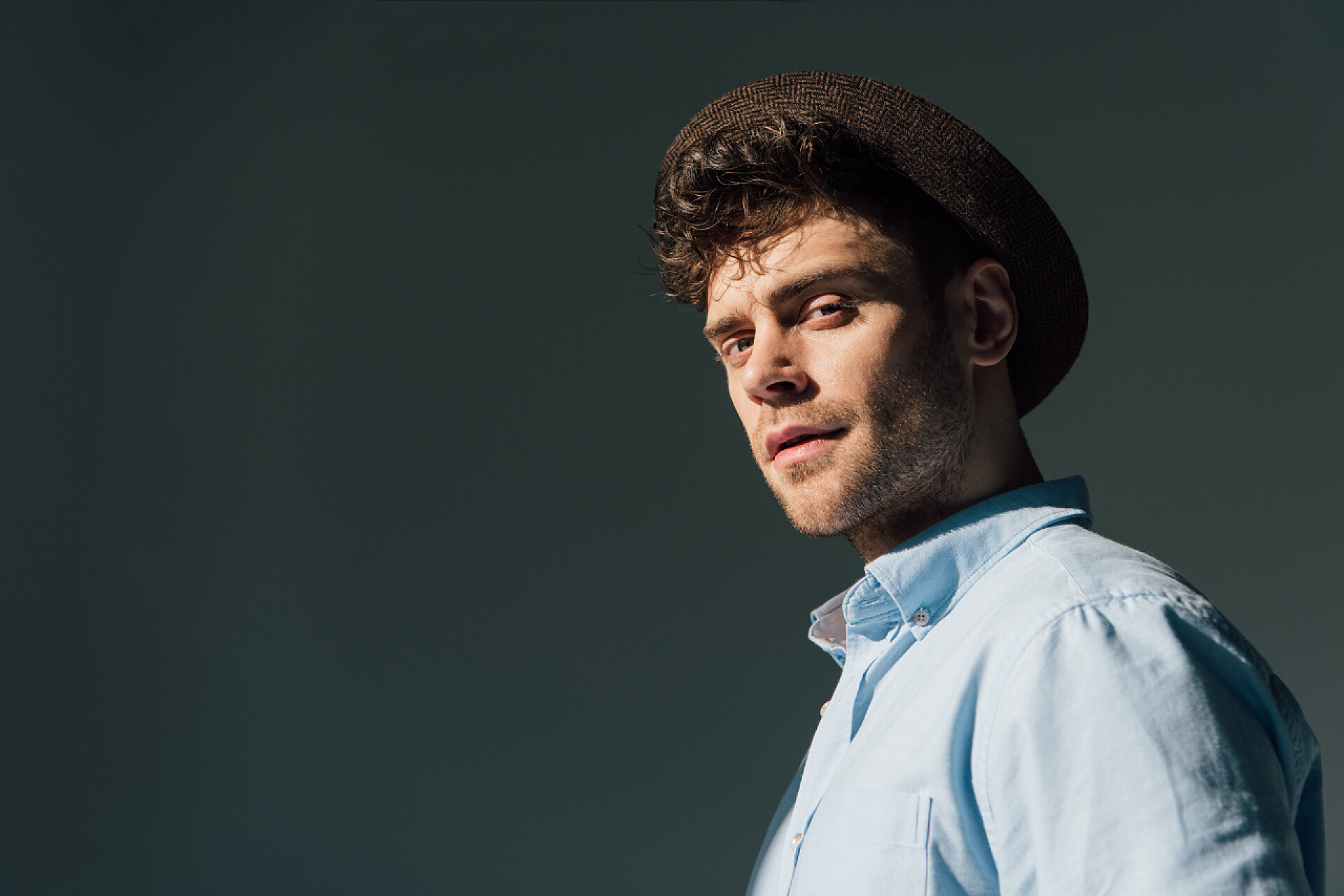 在黑色背景下的一个英俊的男人看着镜头英俊严肃的男人在棕色帽子站在阳光下 