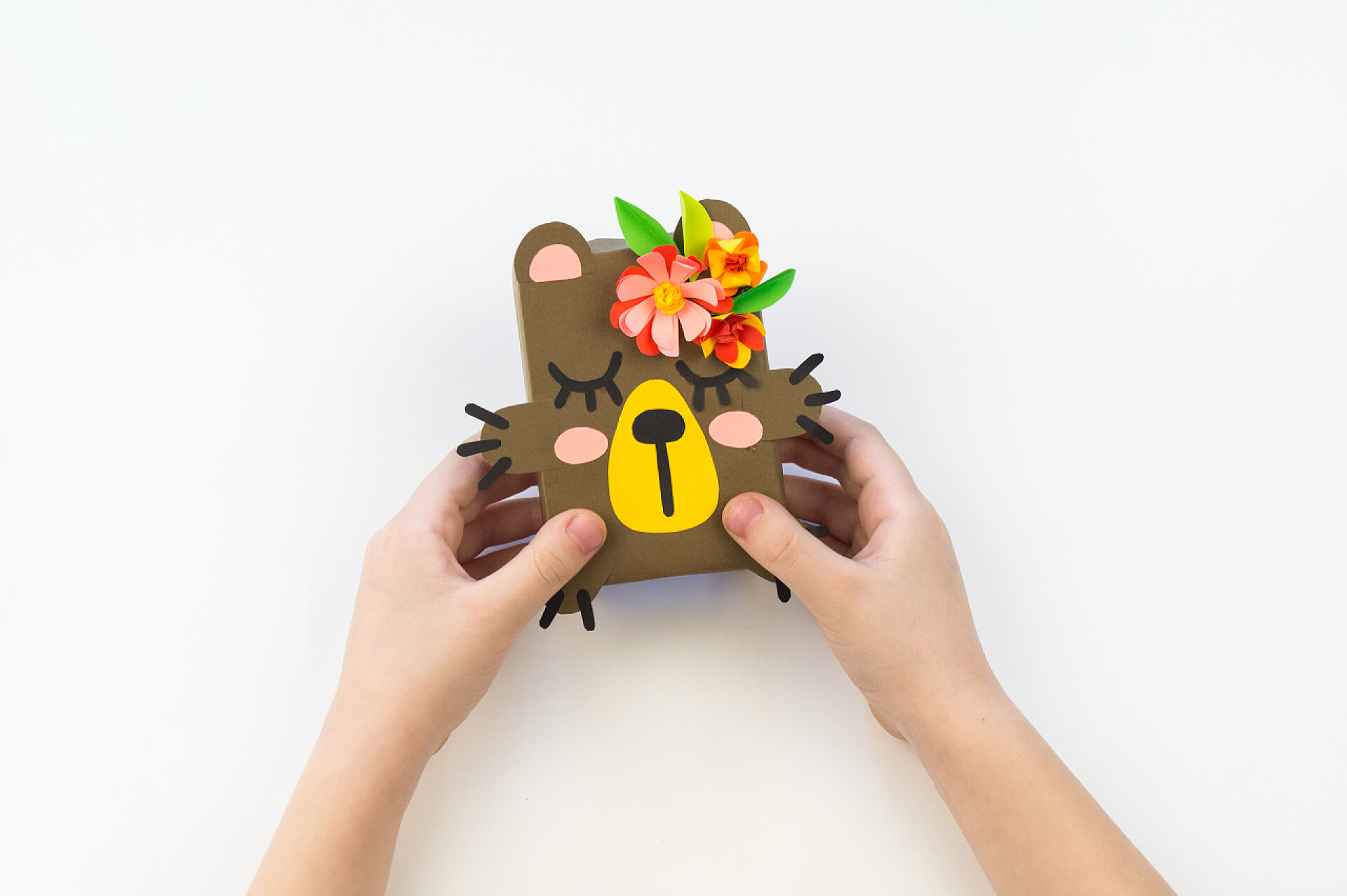 在白色的桌子上一个手拿手工小熊的双手那孩子拿着一只用纸做的熊。儿童工艺品.