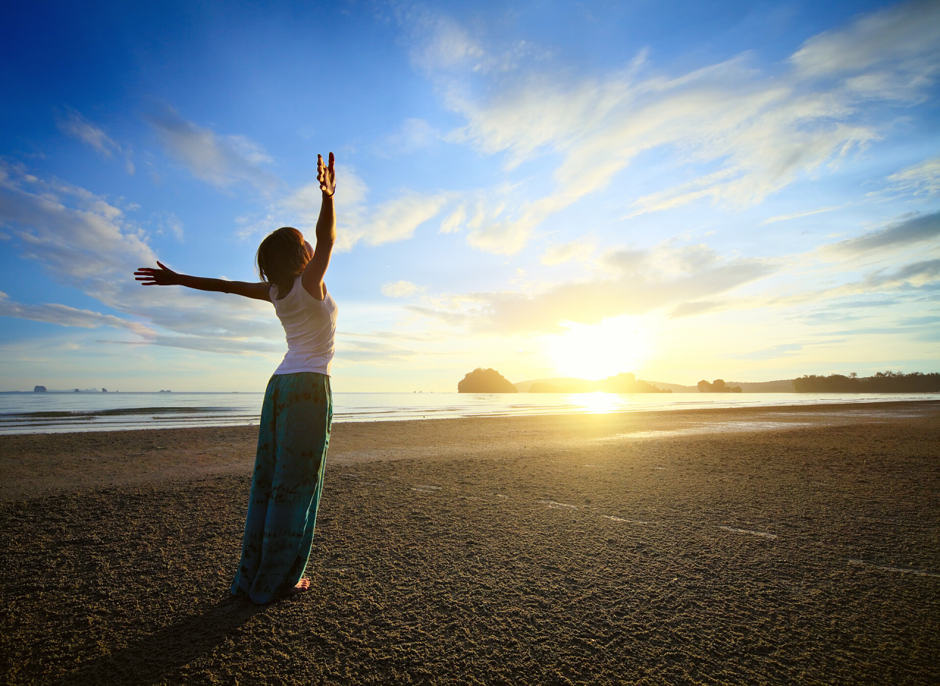 一个女人站在海滩上双手举起拥抱太阳妇女