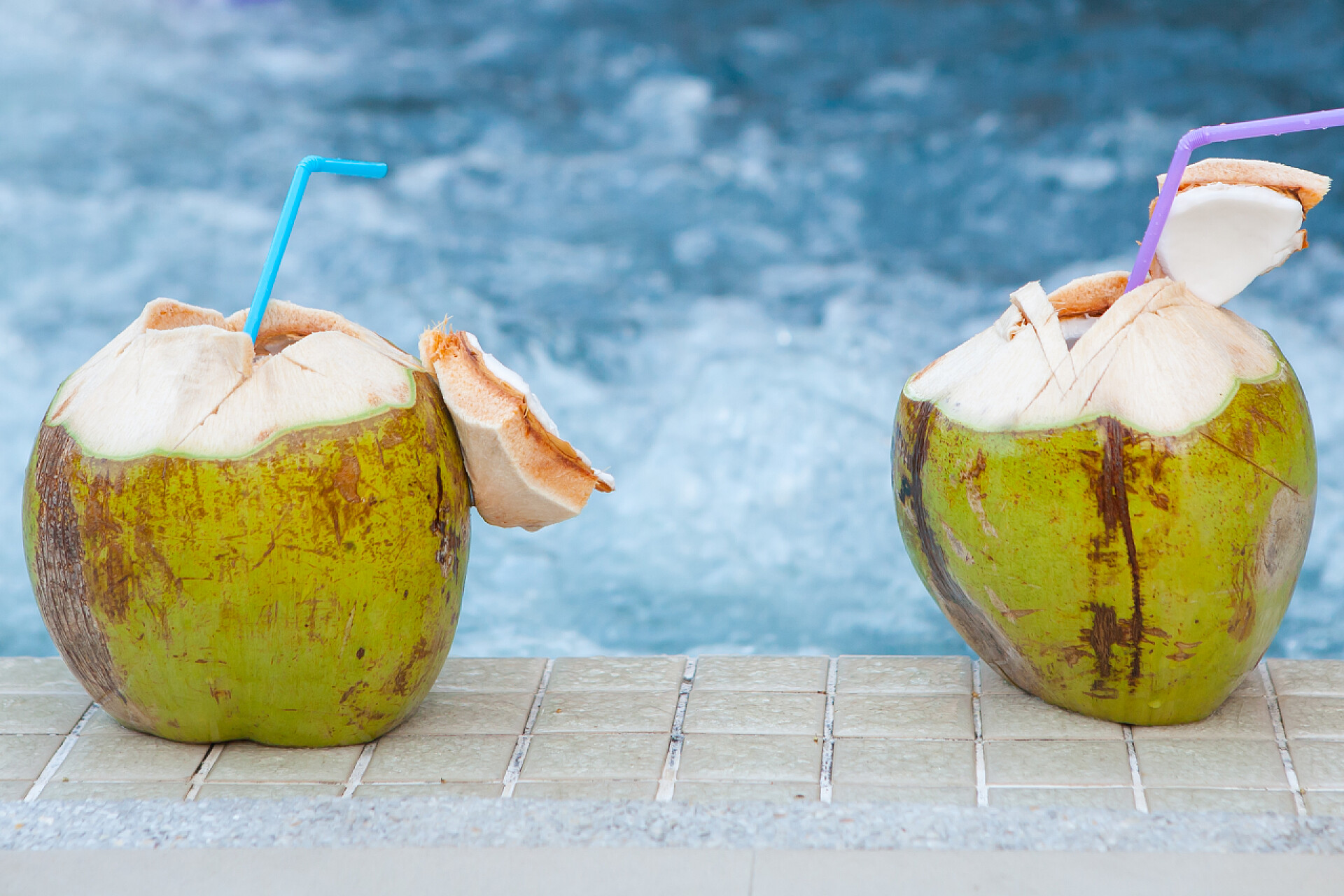 两个椰子在泳池边的特写秸秆在游泳池边喝椰子 