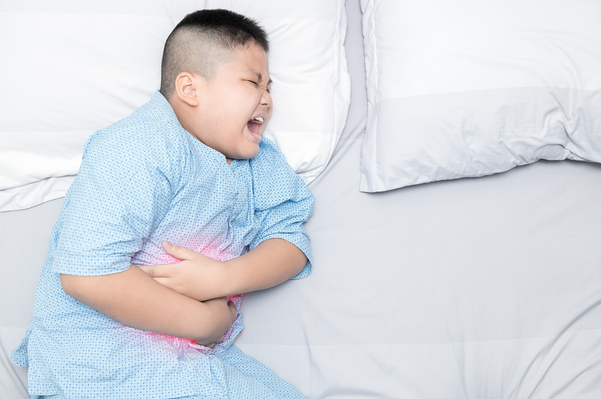 一个小男孩躺在床上痛苦的捂着肚子男孩患肚子疼得在床上