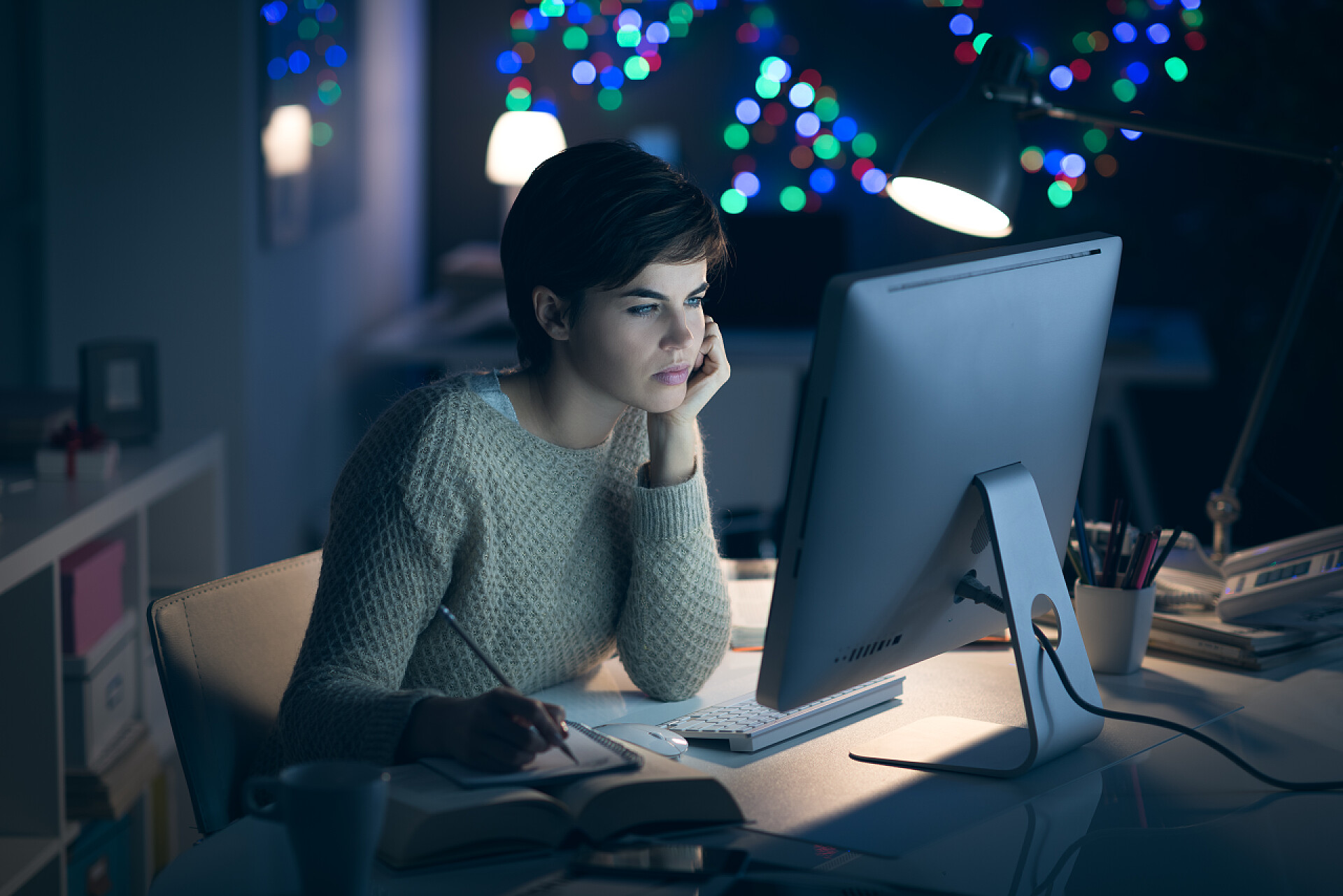 一个女人深夜在电脑前加班深夜工作和学习的年轻女子, 她正在与她的电脑连接, 并在记事本上写下笔记
