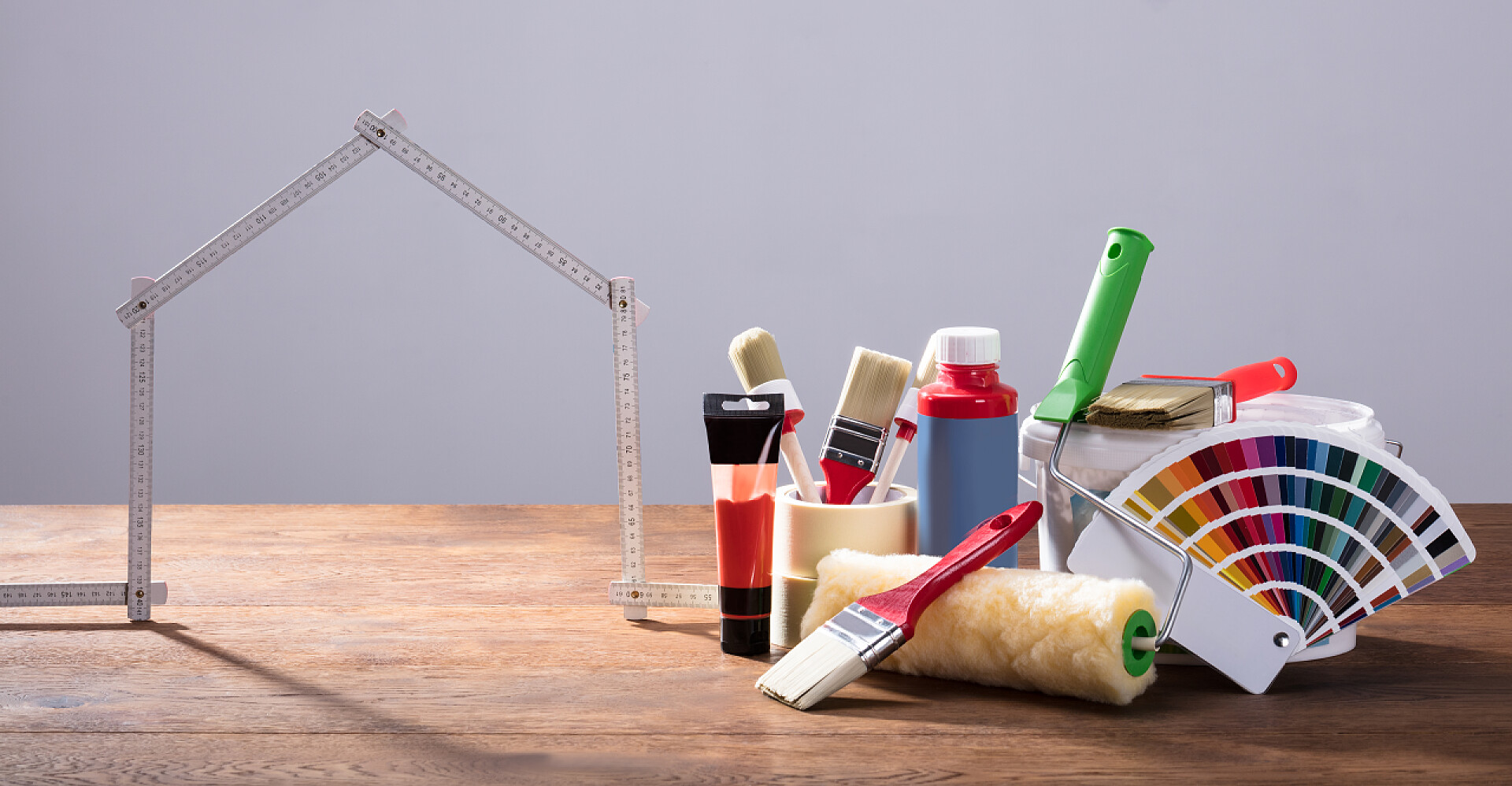 桌子上的房屋装修工具用不同的涂装设备在木桌上用灰色背景测量房子胶带