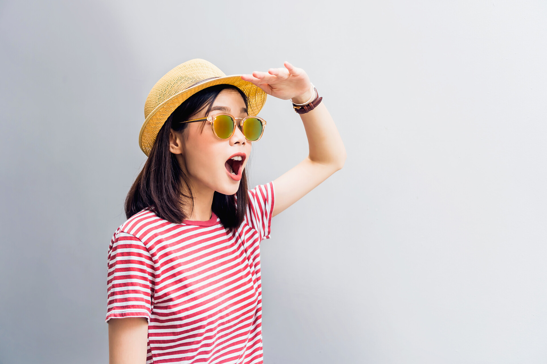 灰色背景上的小女孩带着草帽和墨镜向远处看年轻的女孩高兴地期待着找到一些东西。戴上太阳镜, 反射阳光。概念暑期旅游.