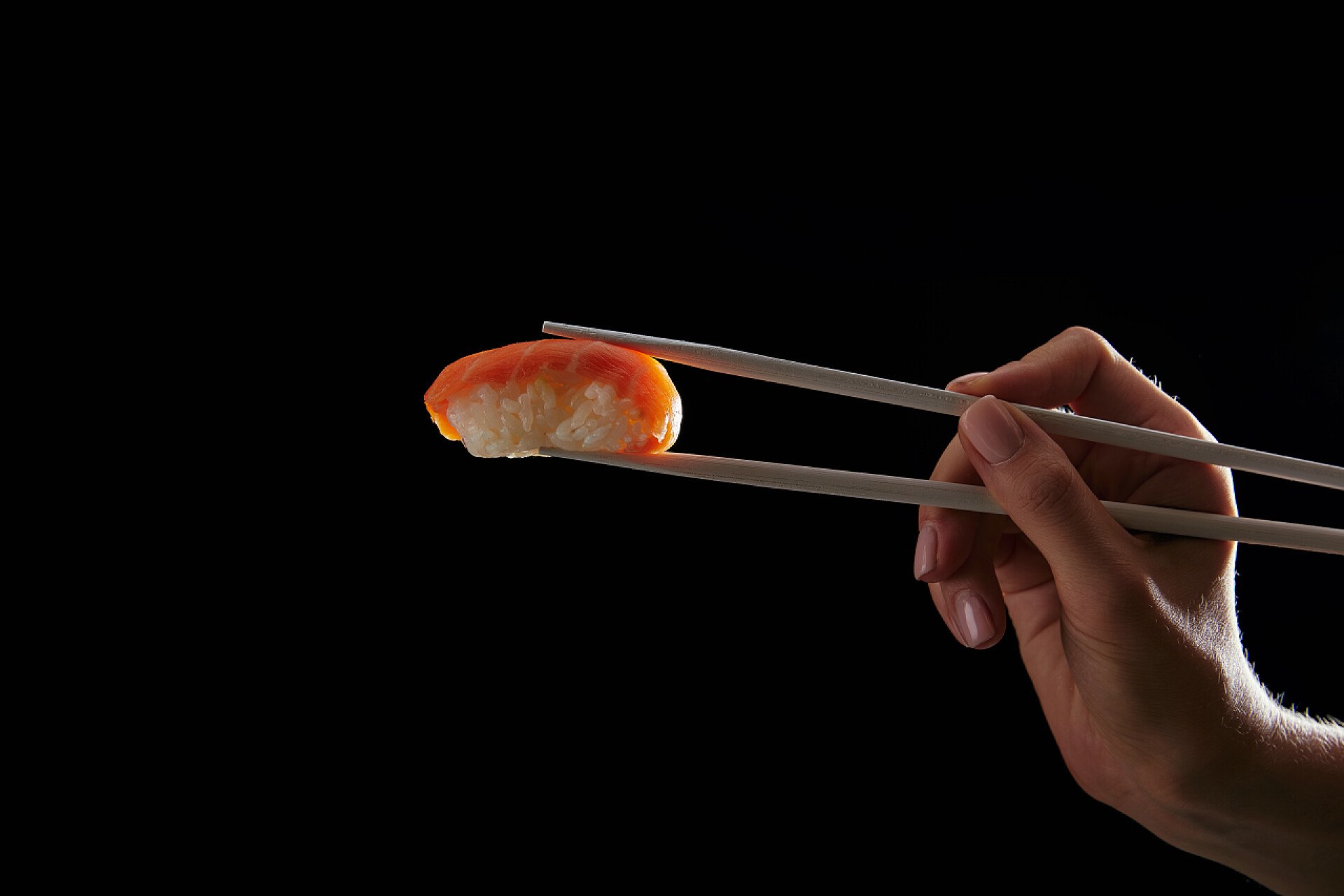 黑色背景筷子夹着寿司妇女举行握寿司与鲑鱼分离黑色的热