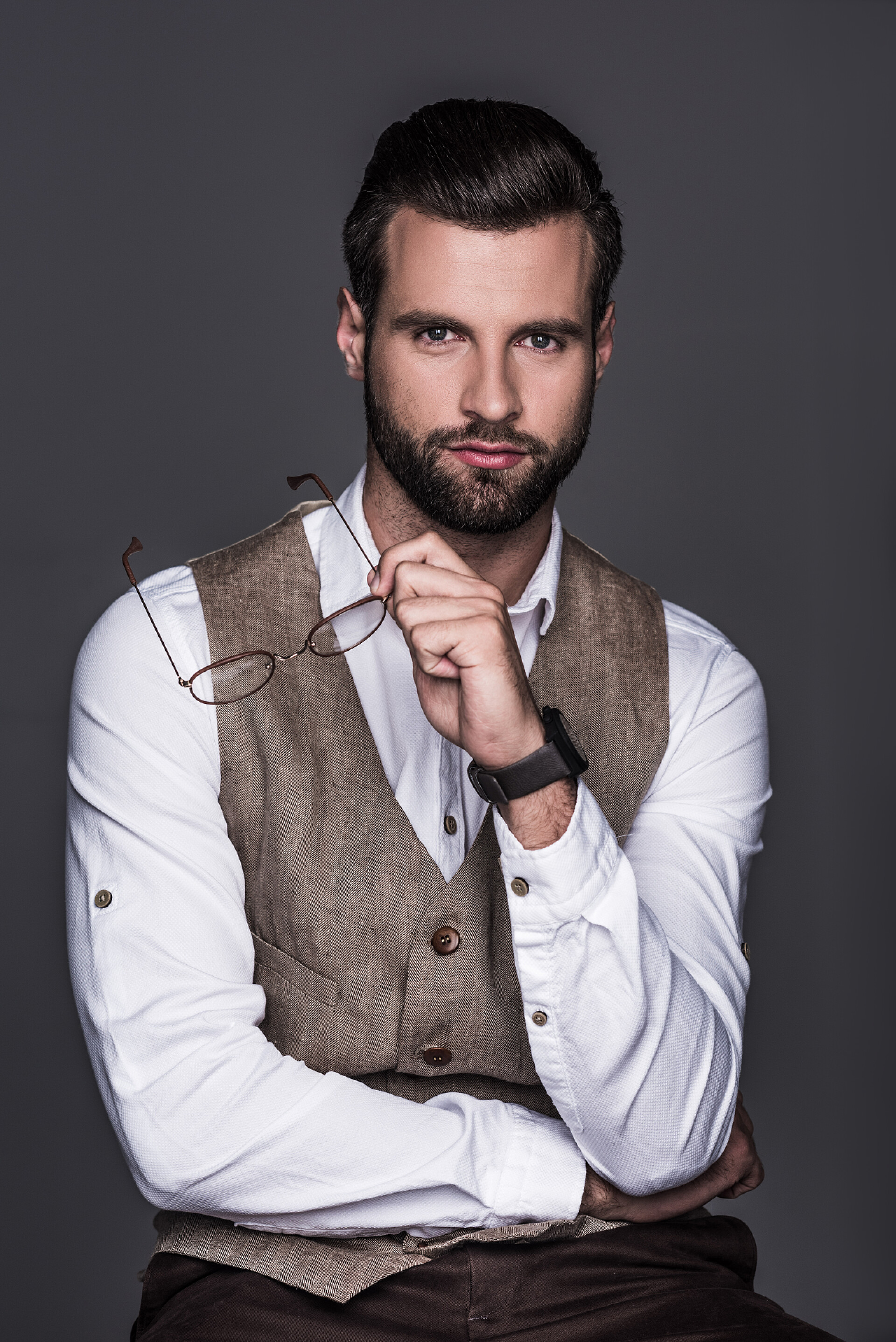 灰色背景上一个成功商人时尚男子的肖像手持眼镜和摆在优雅的背心, 孤立的灰色 