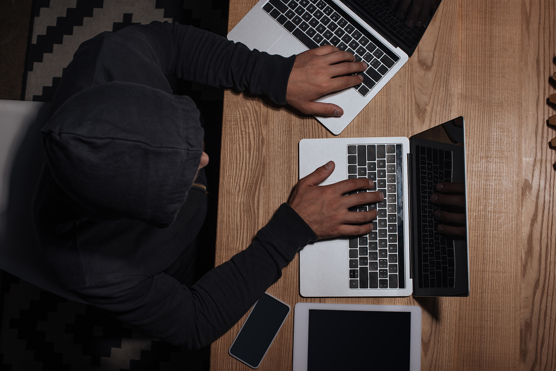 俯拍黑客玩笔记本电脑黑客在黑色连帽的头顶视图使用笔记本电脑在桌面与平板电脑和智能手机, 网络安全概念