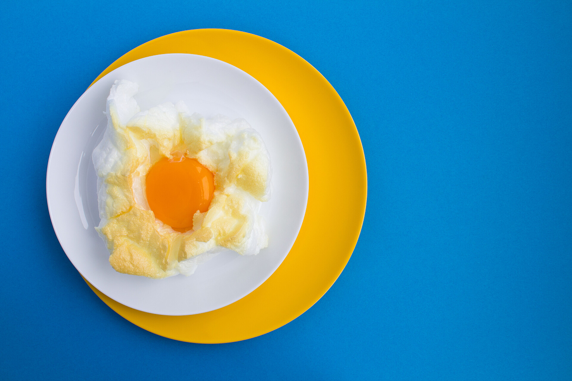 蓝色背景上一碟煎鸡蛋鸡蛋在云中的五颜六色的盘子在蓝色的背景。顶部视图。复制空间.