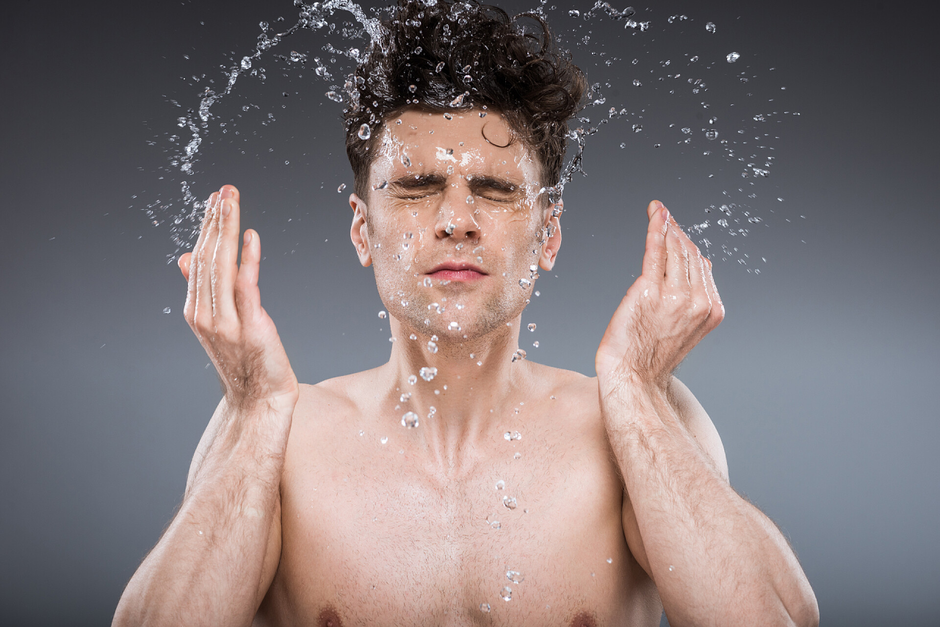 灰色背景中一个男人正在洗脸英俊的男人溅入脸的水, 隔离在灰色