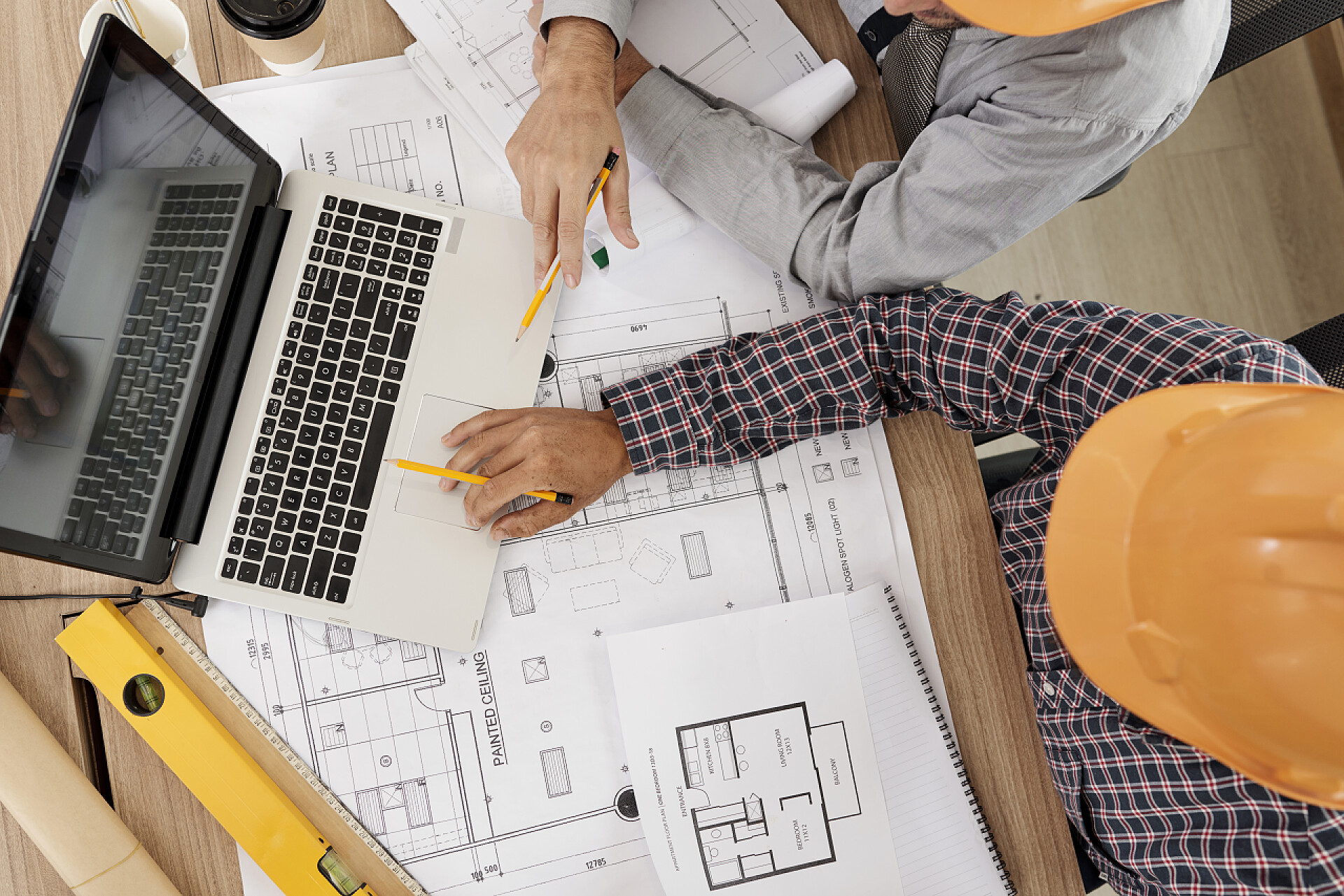 两个建筑工程师讨论项目建筑工程师聚集在有纸质蓝图的笔记本电脑上讨论项目