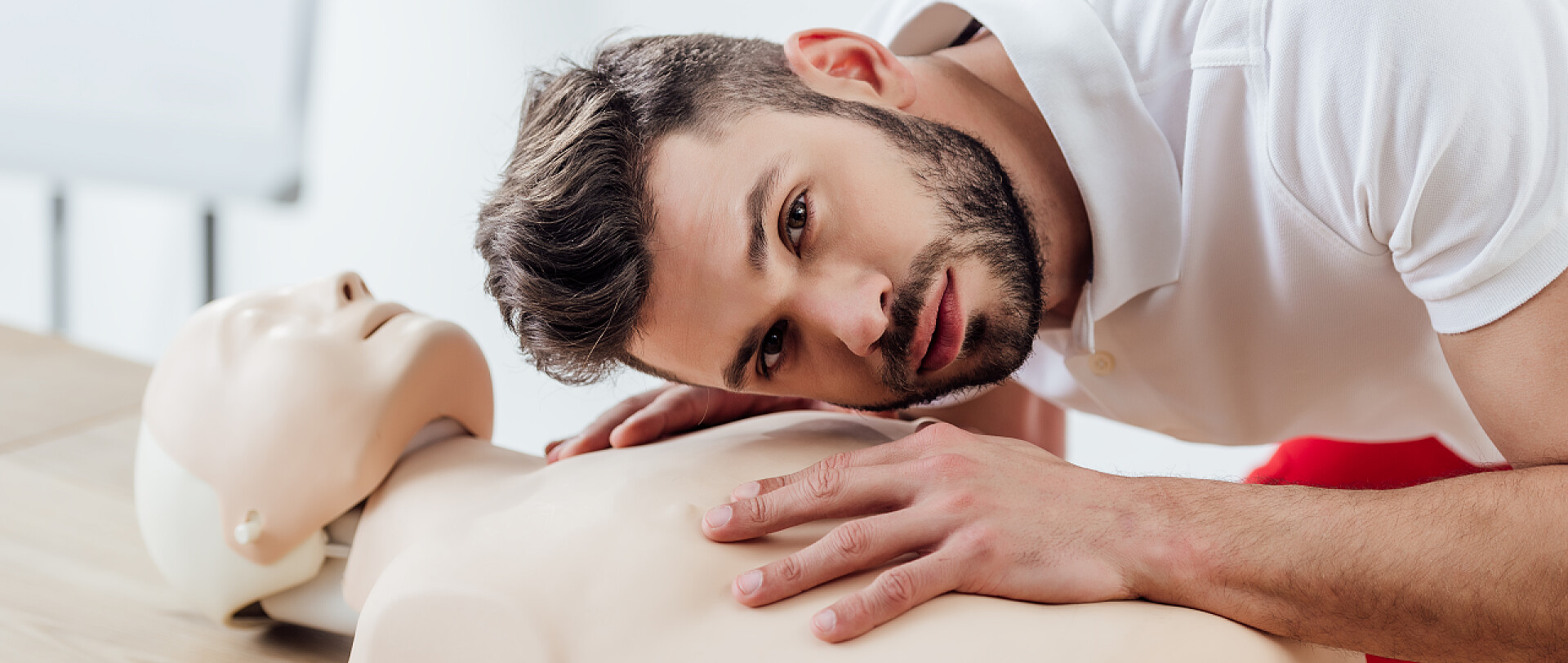 穿白色体恤的男人在听假人的心跳在急救训练中, 男子在假人身上观看镜头和练习 cpr 技术的全景照片