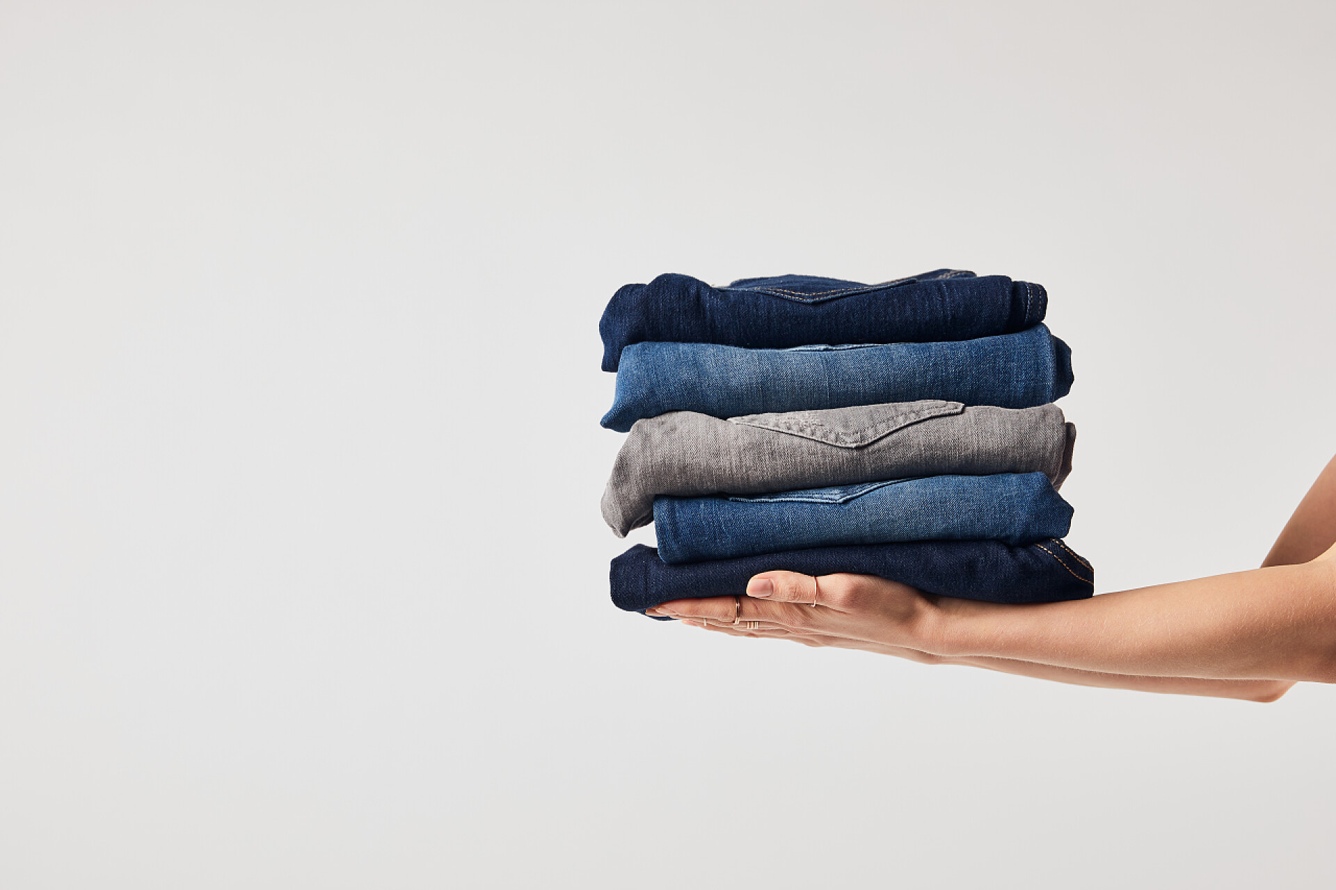 灰色背景一堆叠放整齐的衣物女孩拿着熨烫的裤子的裁剪的看法查出在白色