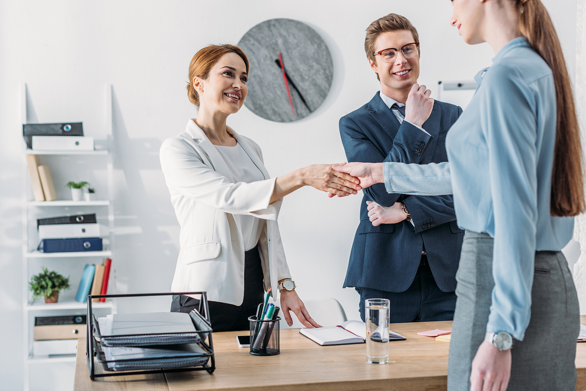 面试的蓝衣女性与面试官愉快的握手与愉快的招聘人员在漂亮的同事附近戴眼镜的妇女握手的裁剪视图