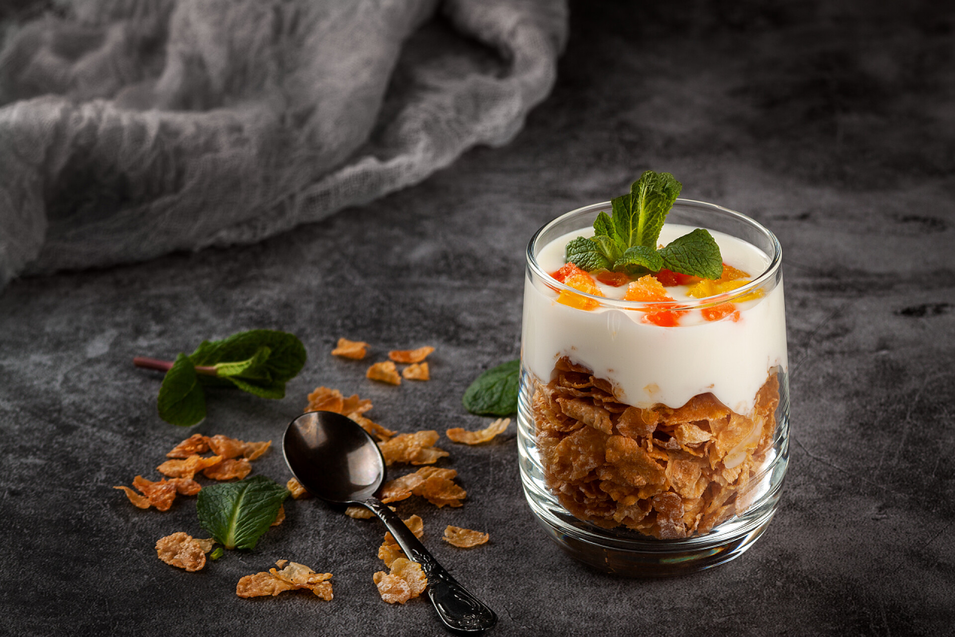 玻璃瓶中的奶酪甜点在深灰色背景的玻璃杯中的玉米片