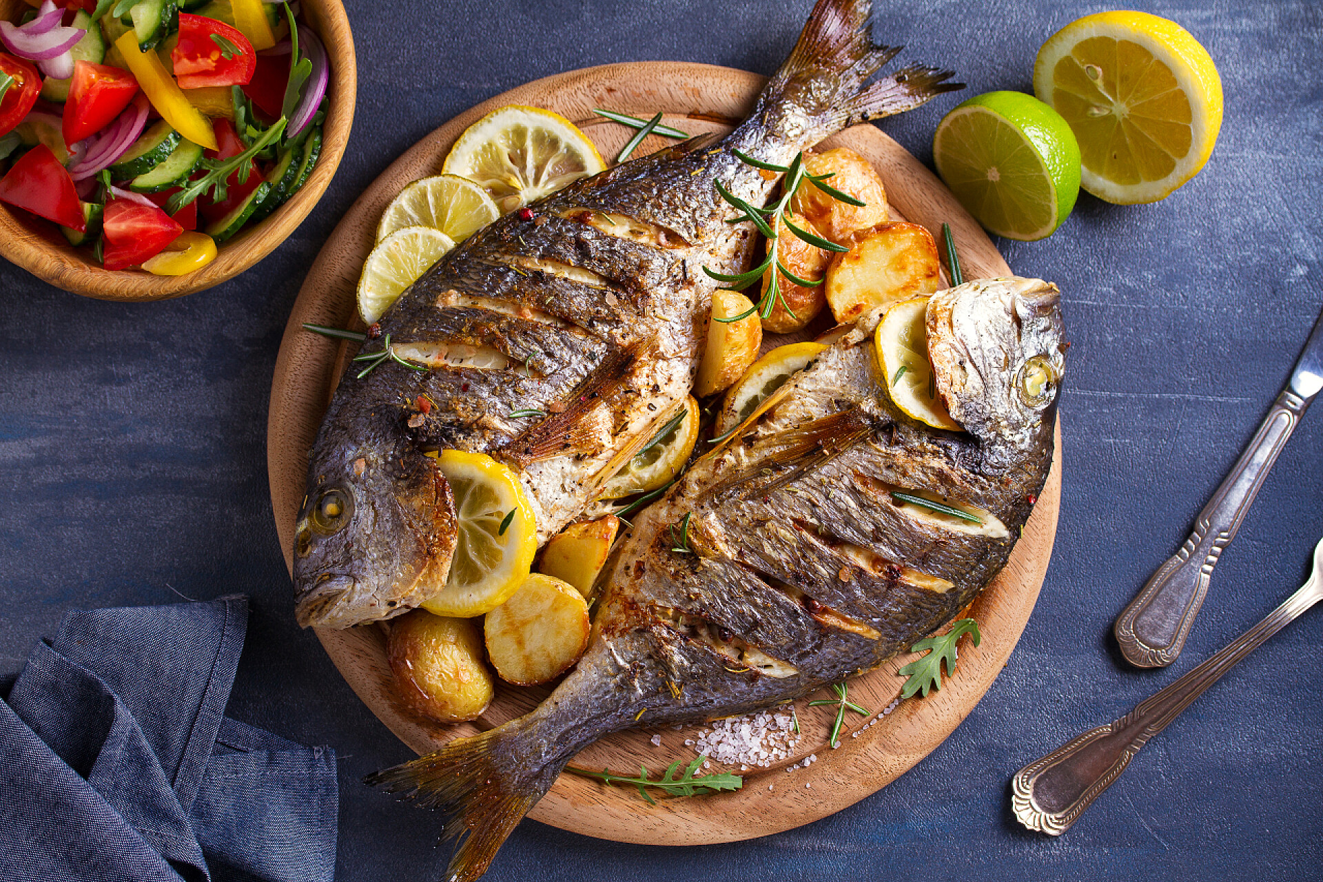 盘子里的油炸鱼食物烤鱼配烤土豆、柠檬和木托盘上的迷迭香。从上面看, 顶部