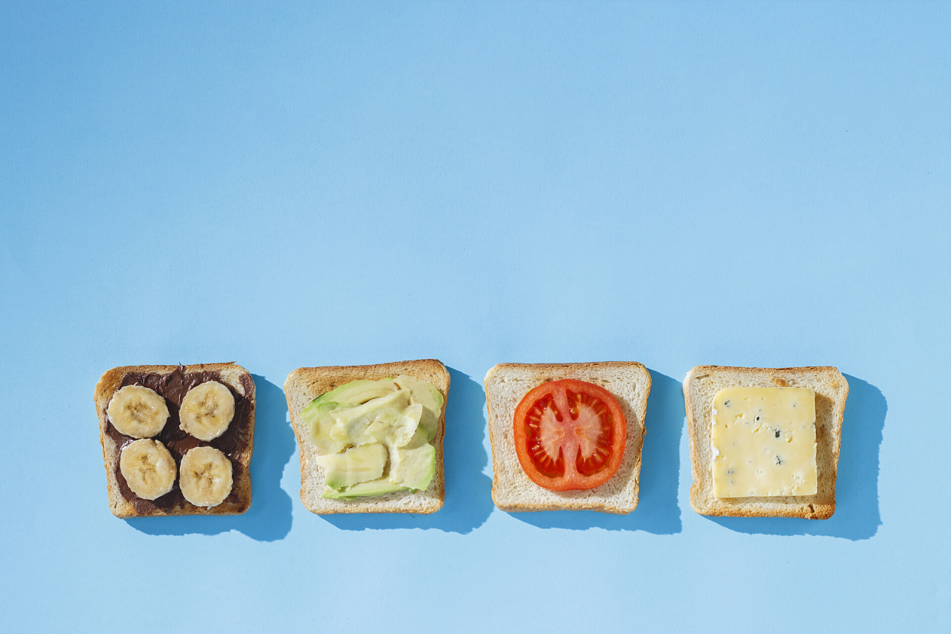 蓝色背景上美味的奶酪三明治三明治与奶酪，番茄，香蕉和鳄梨在蓝色背景。健康饮食的理念，酒店早餐，饮食。自然采光，硬光。平铺，顶视图.