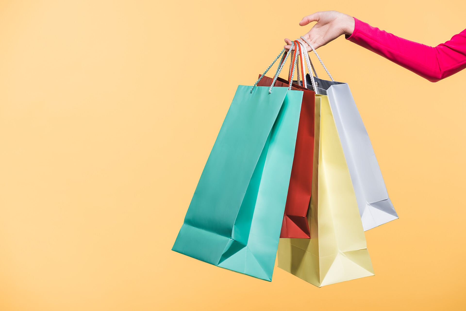 黄色背景上拿着购物袋的年轻女人手部特写裁剪视图的妇女与购物袋，隔离在黄色