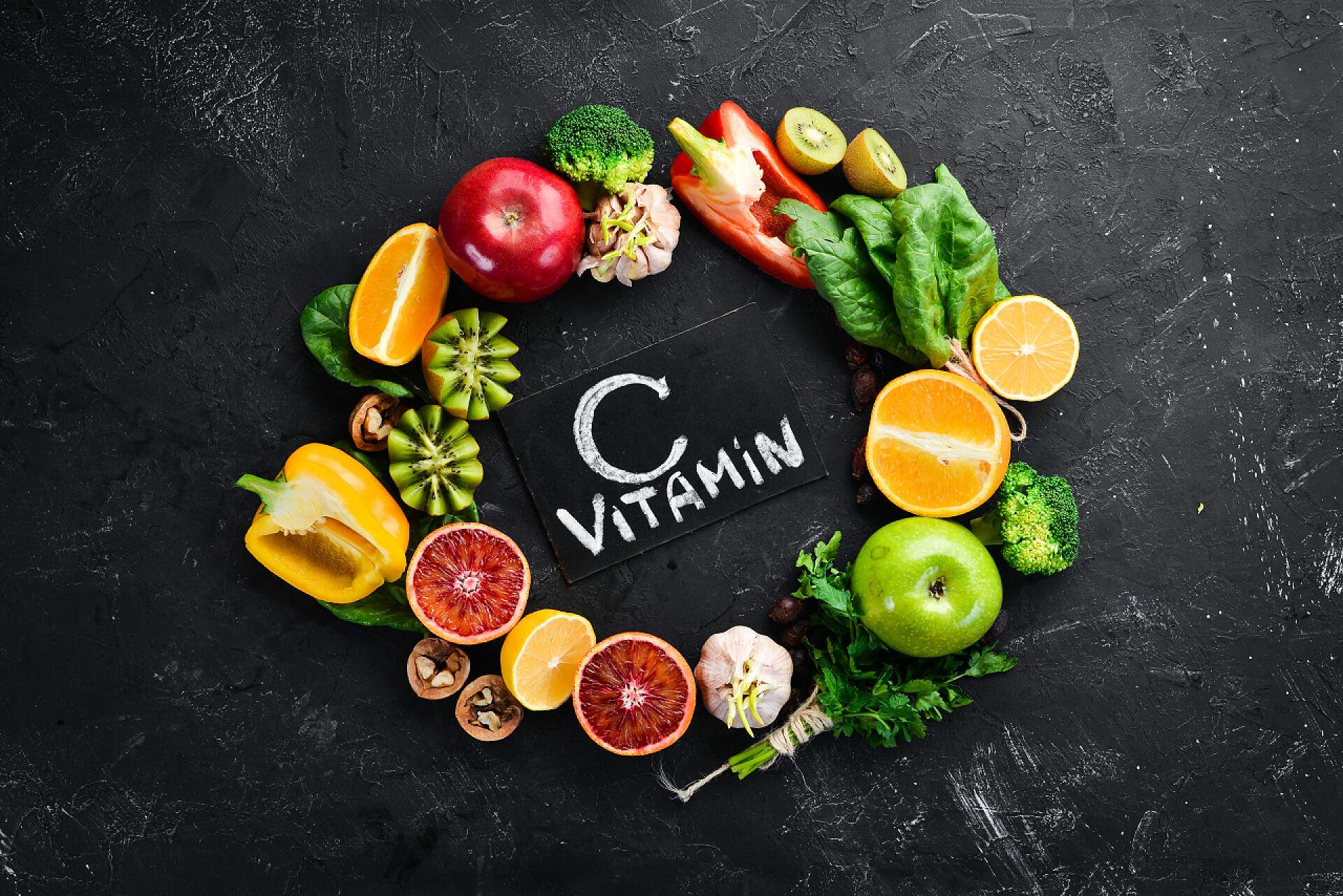 富含维生素c的水果蔬菜特写含有维生素C的水果和蔬菜：橙子、柠檬、苹果、玫瑰、大蒜、花椰菜、苹果、奇异果、菠菜。顶部视图。在黑色的石头背景上.