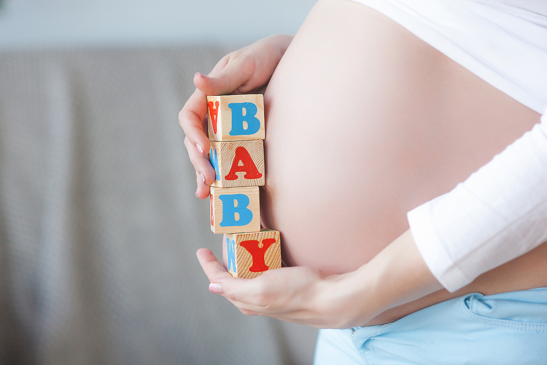 孕妇拿着baby的英文字母年轻的孕妇在室内。 女人期待的特写。 漂亮的女性在等着她的小宝宝出生.